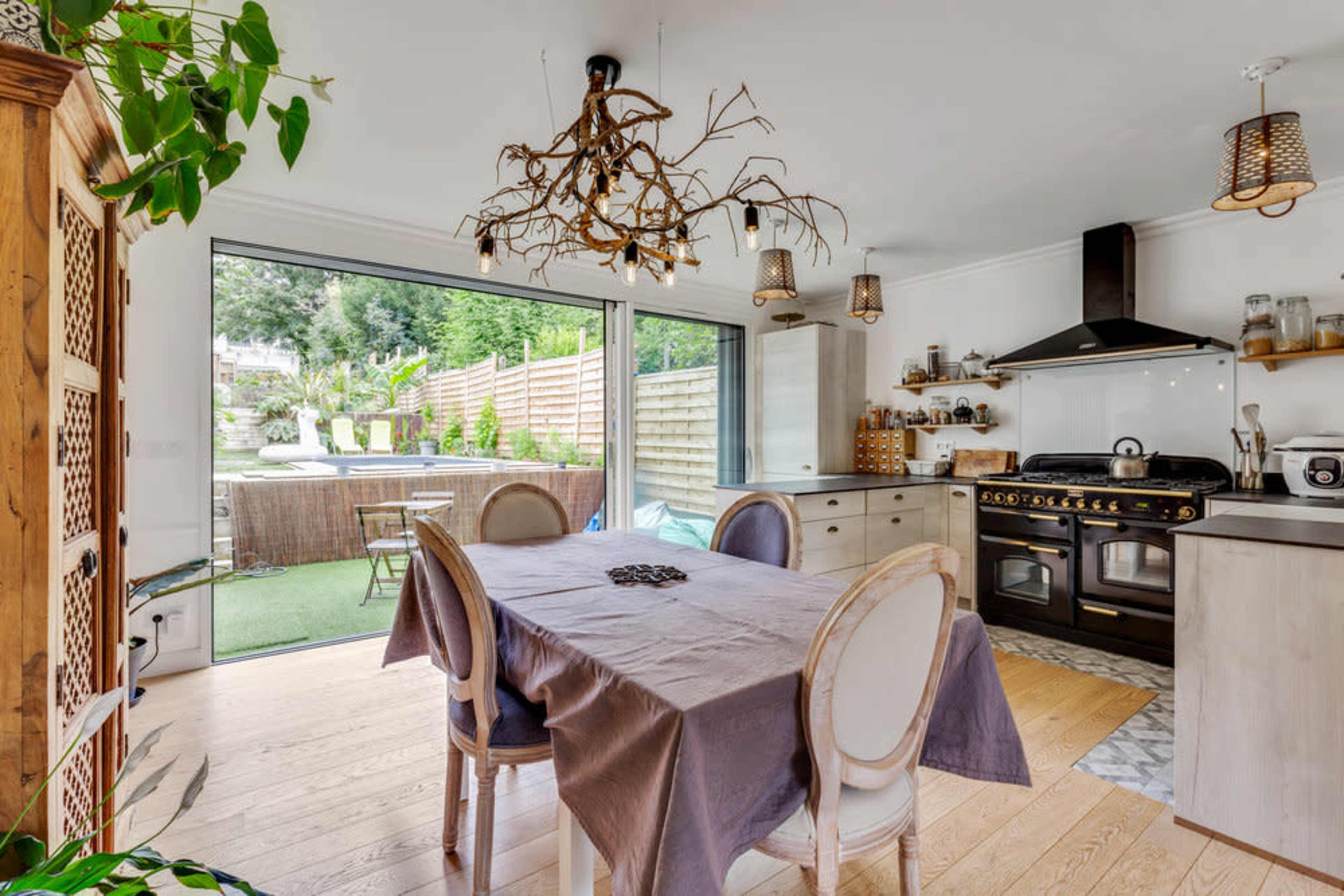 A modern kitchen-dining area features a wooden table surrounded by upholstered chairs, with large glass doors opening to an outdoor seating area.