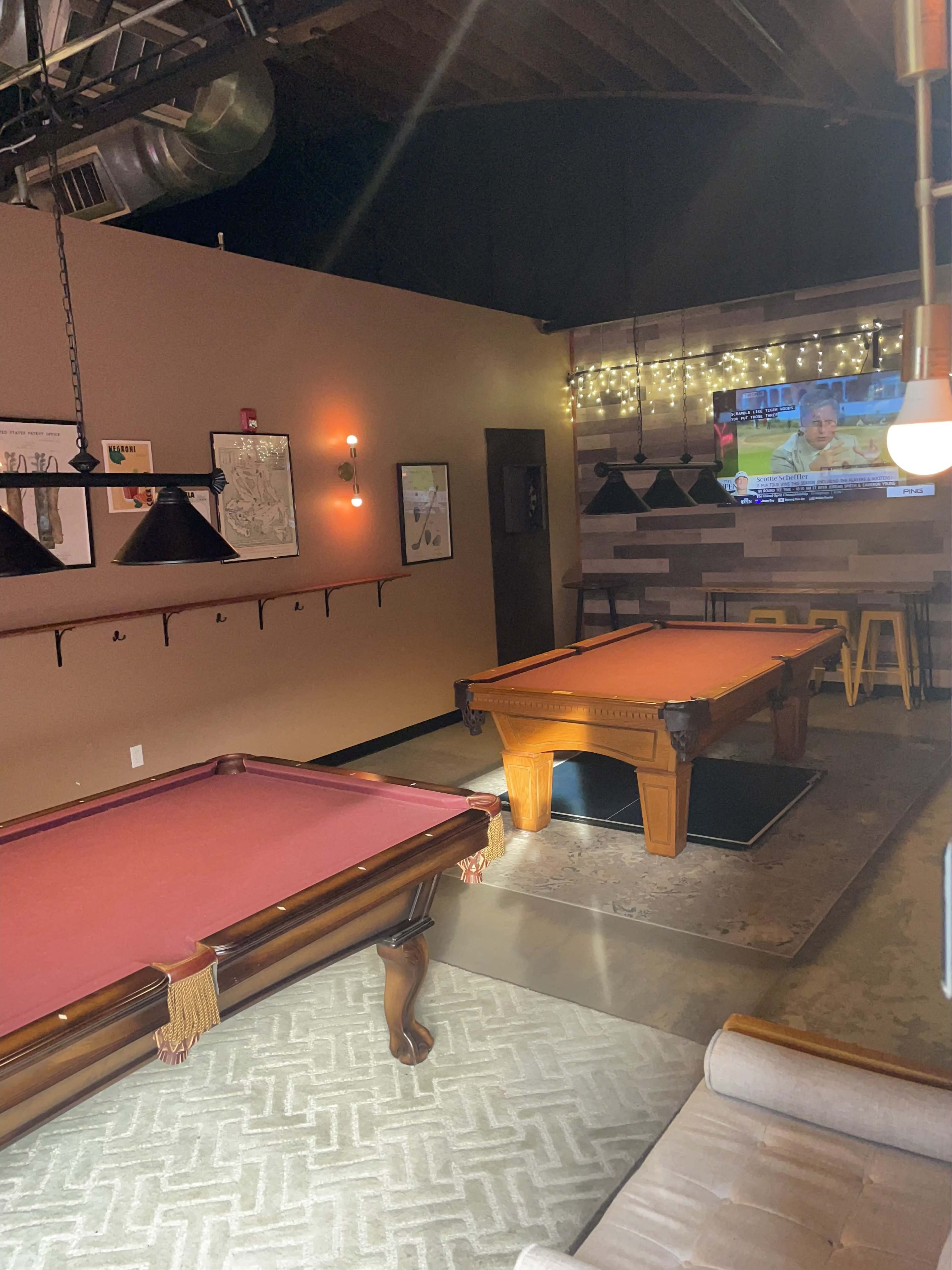 A recreational room featuring a billiard table, a sitting area, and a television mounted on the wall.