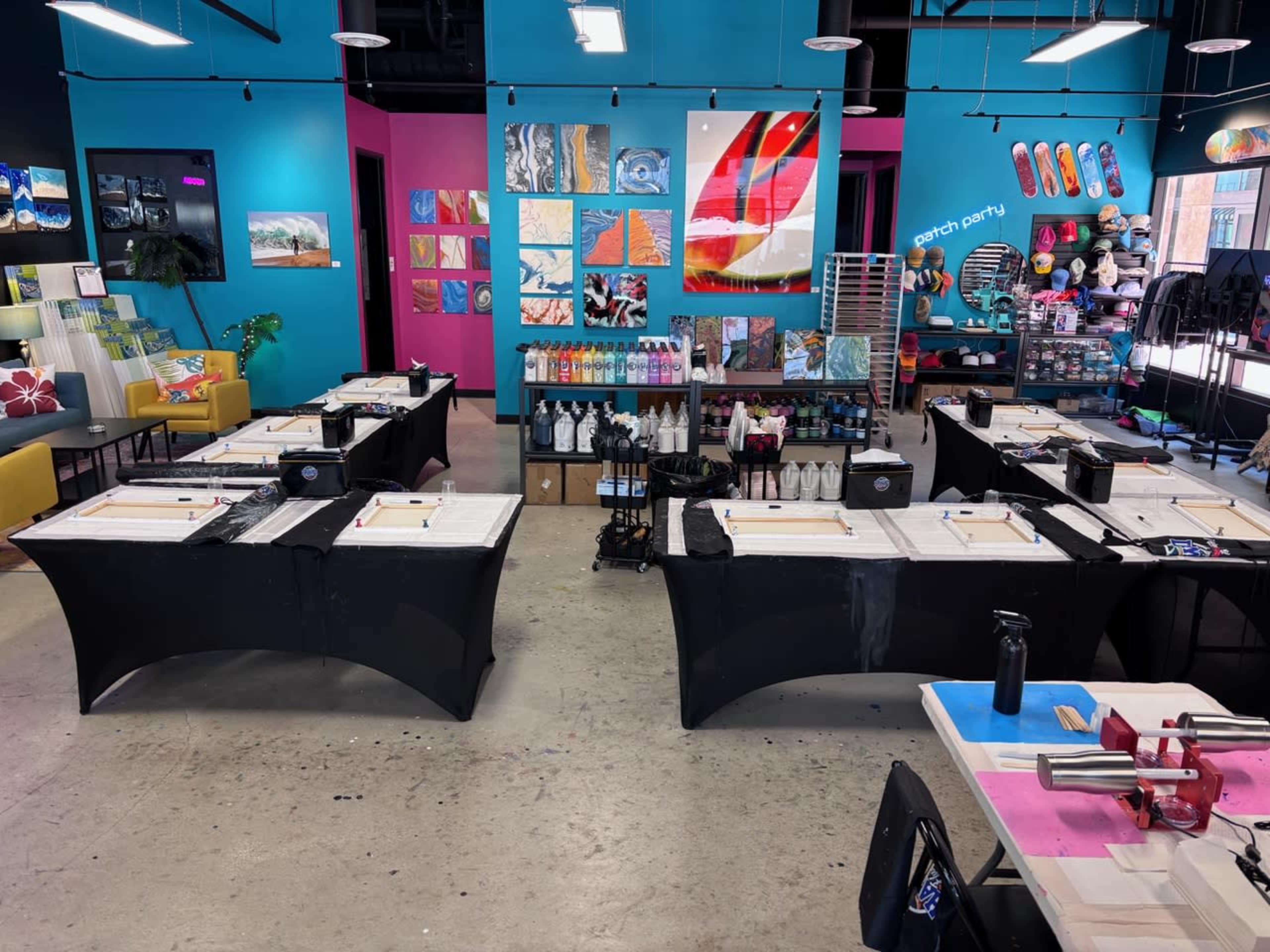 The image shows a brightly colored art studio with several tables set up for painting, surrounded by various artworks displayed on the walls.