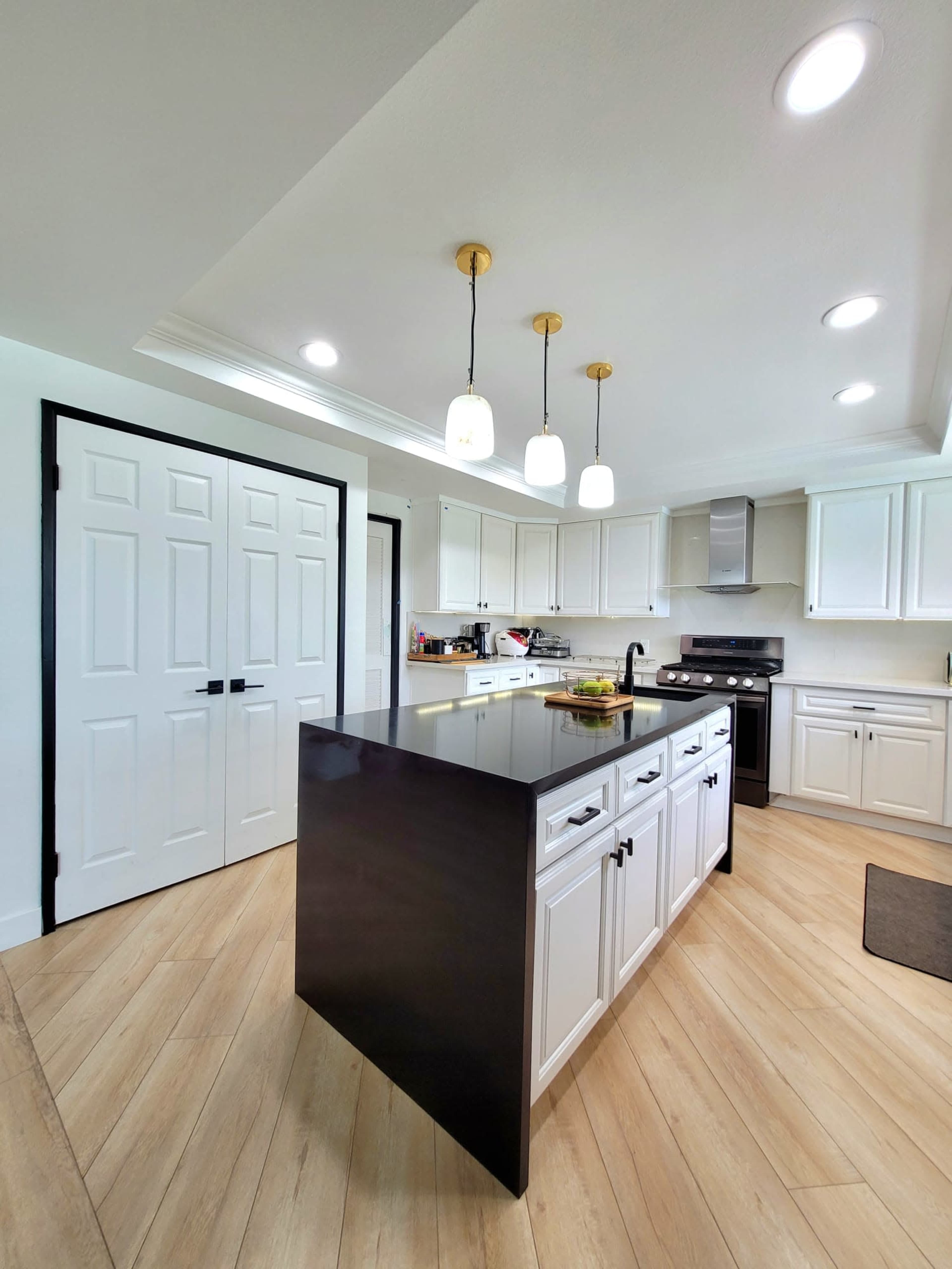 A modern kitchen features a central black island, white cabinetry, and pendant lighting.