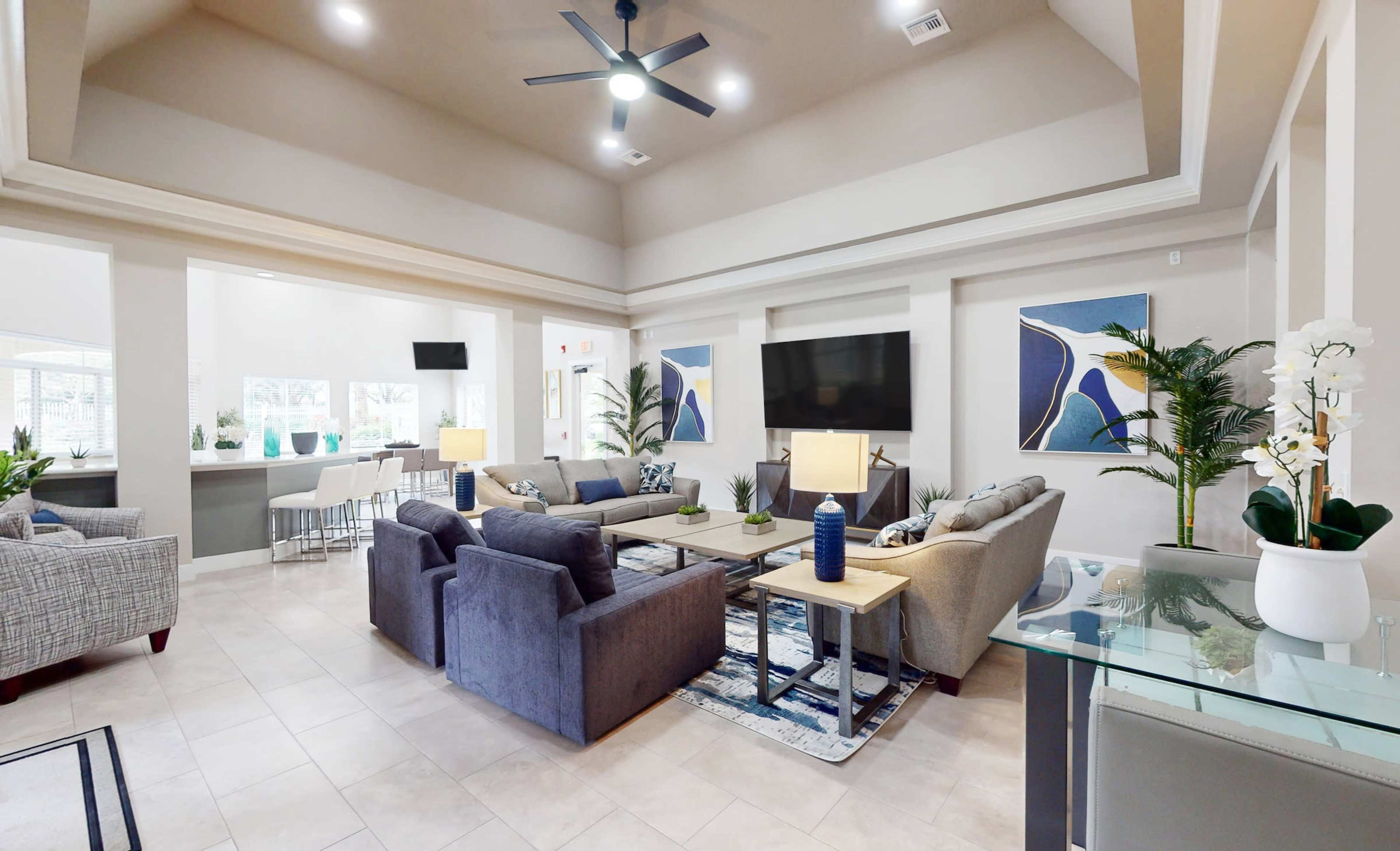 A large, well-lit lounge area with seating arrangements, a coffee table, and decorative plants, along with a television mounted on the wall.