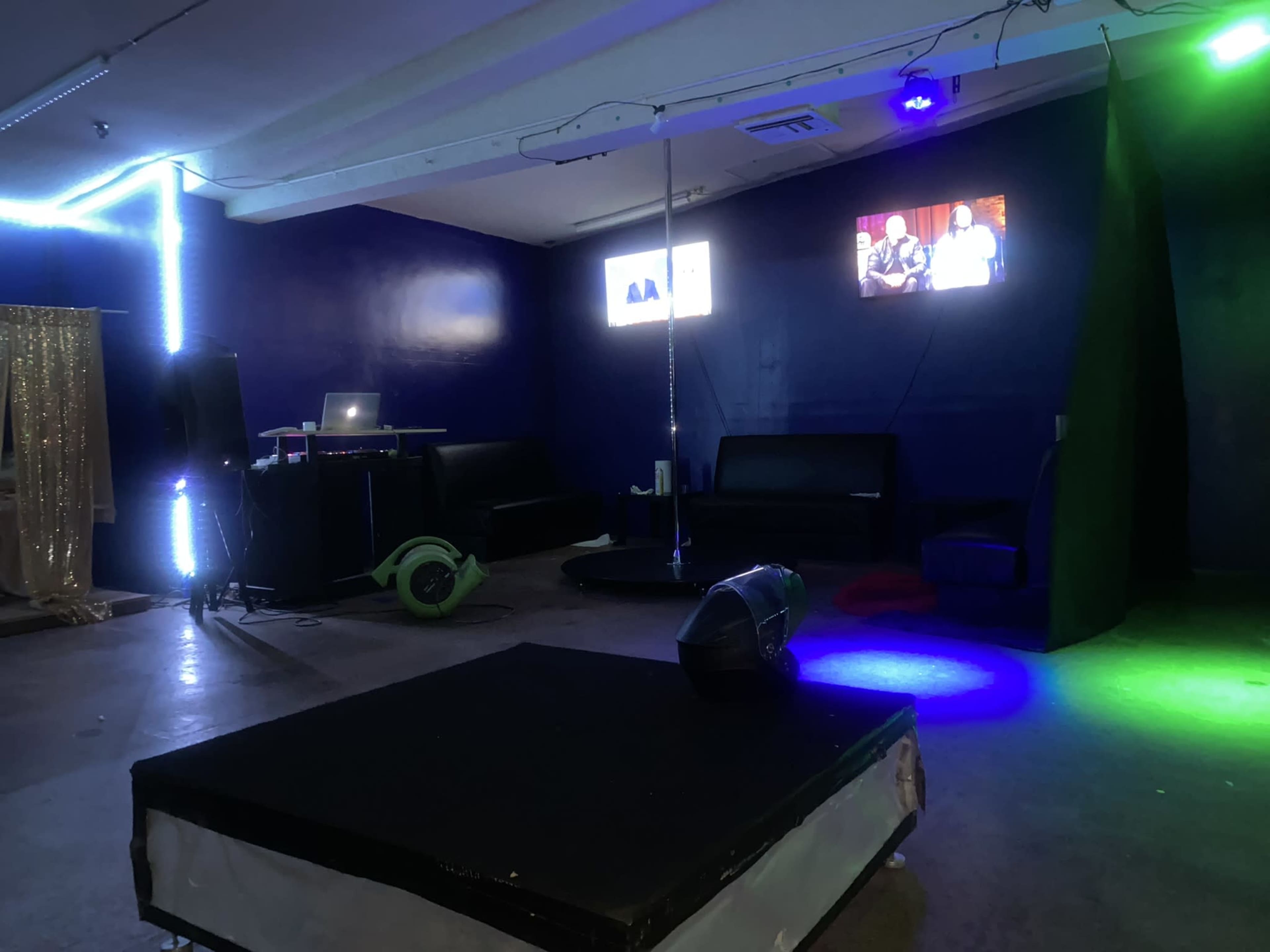 An indoor space with a small stage area, lighting effects, a DJ booth, and seating arrangements.