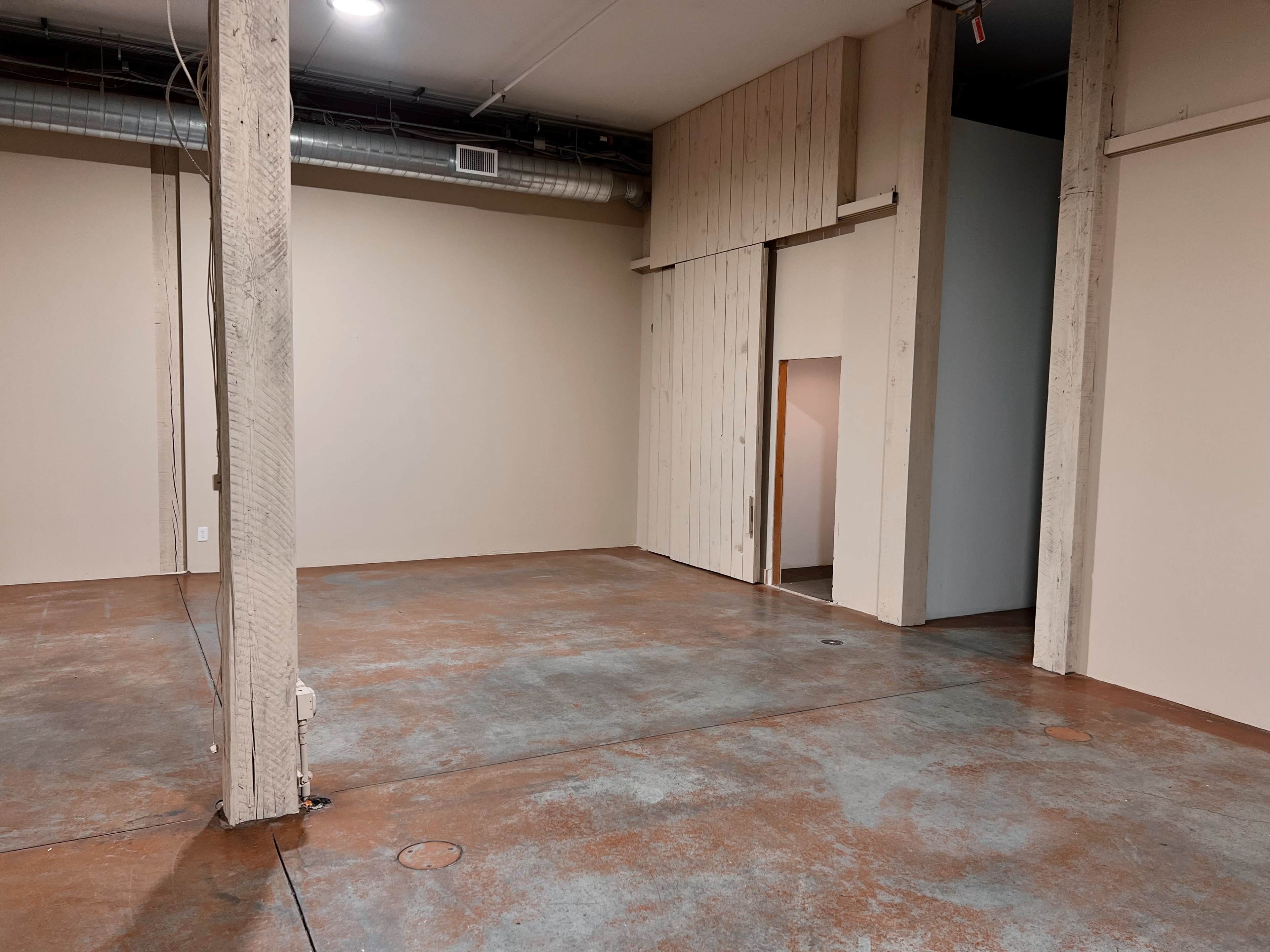 An empty room with concrete flooring, beige walls, and a partially open doorway.