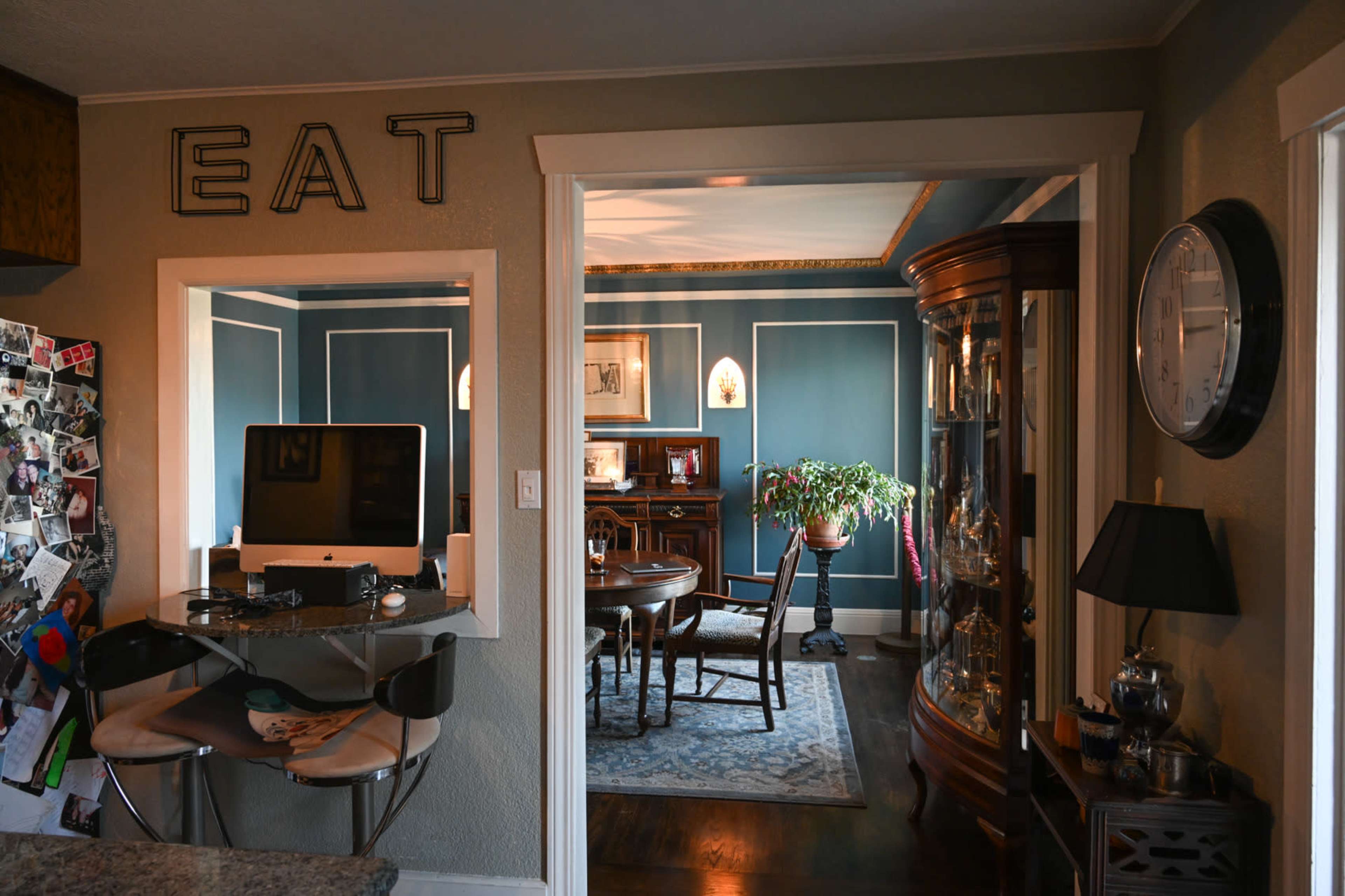 A kitchen area opens to a dining room featuring a circular table and a china cabinet, with a wall sign that says "EAT."