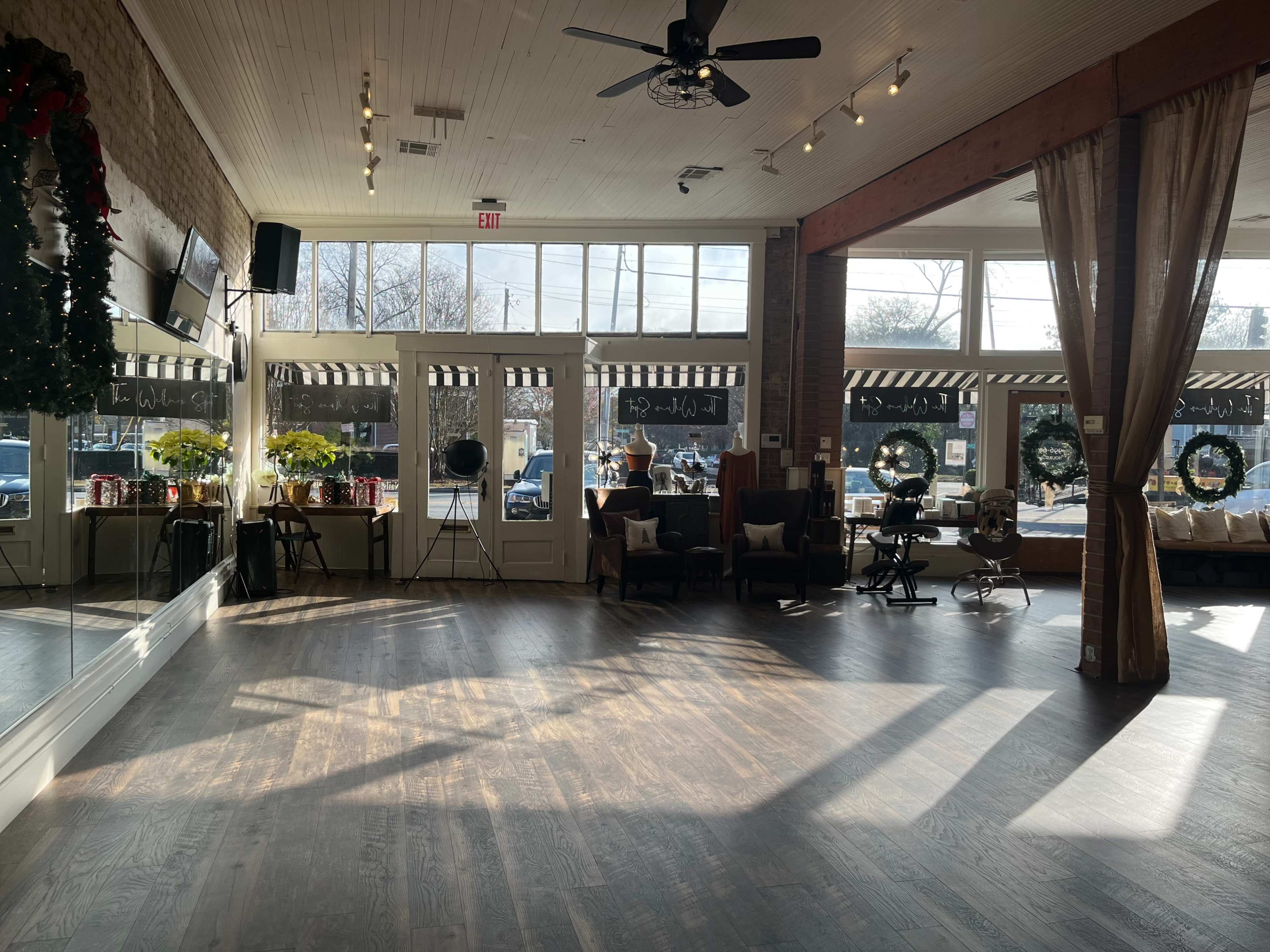 A spacious, well-lit interior of a café or event space with large windows, hardwood flooring, and festive decorations.