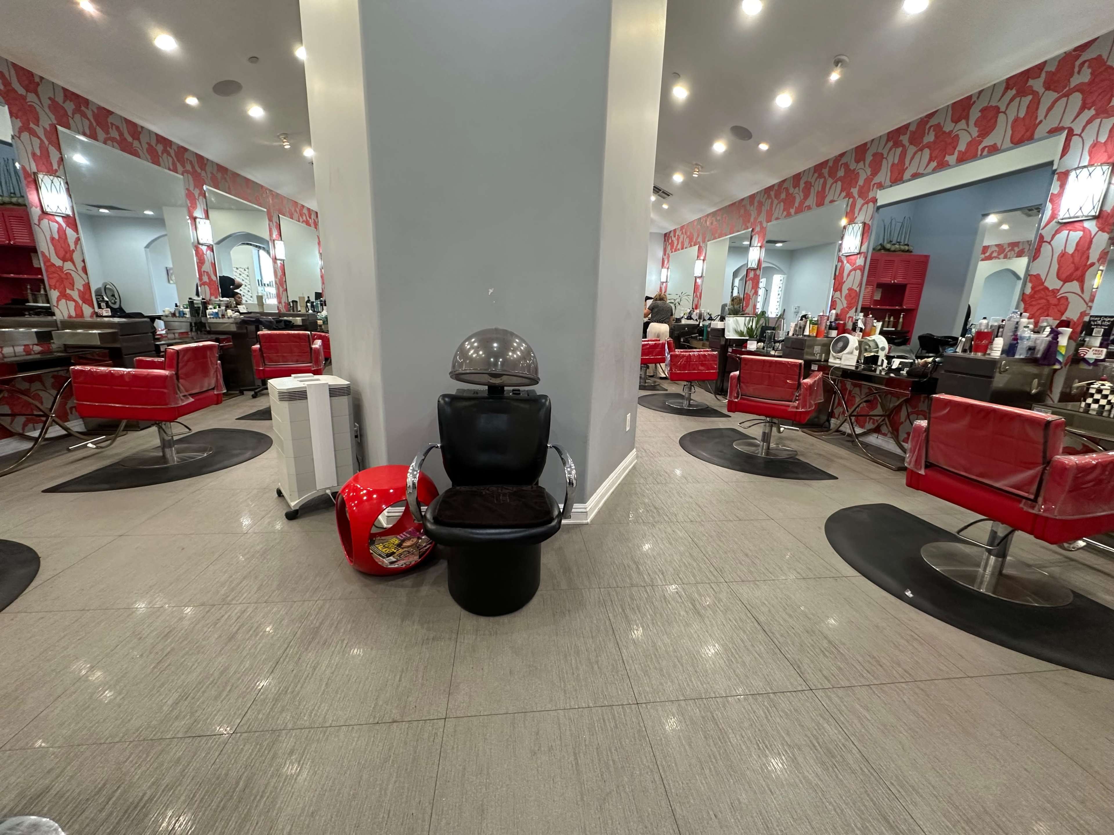 The image shows a hair salon interior with red and black styling chairs, mirrors, and a hair dryer station in the center.