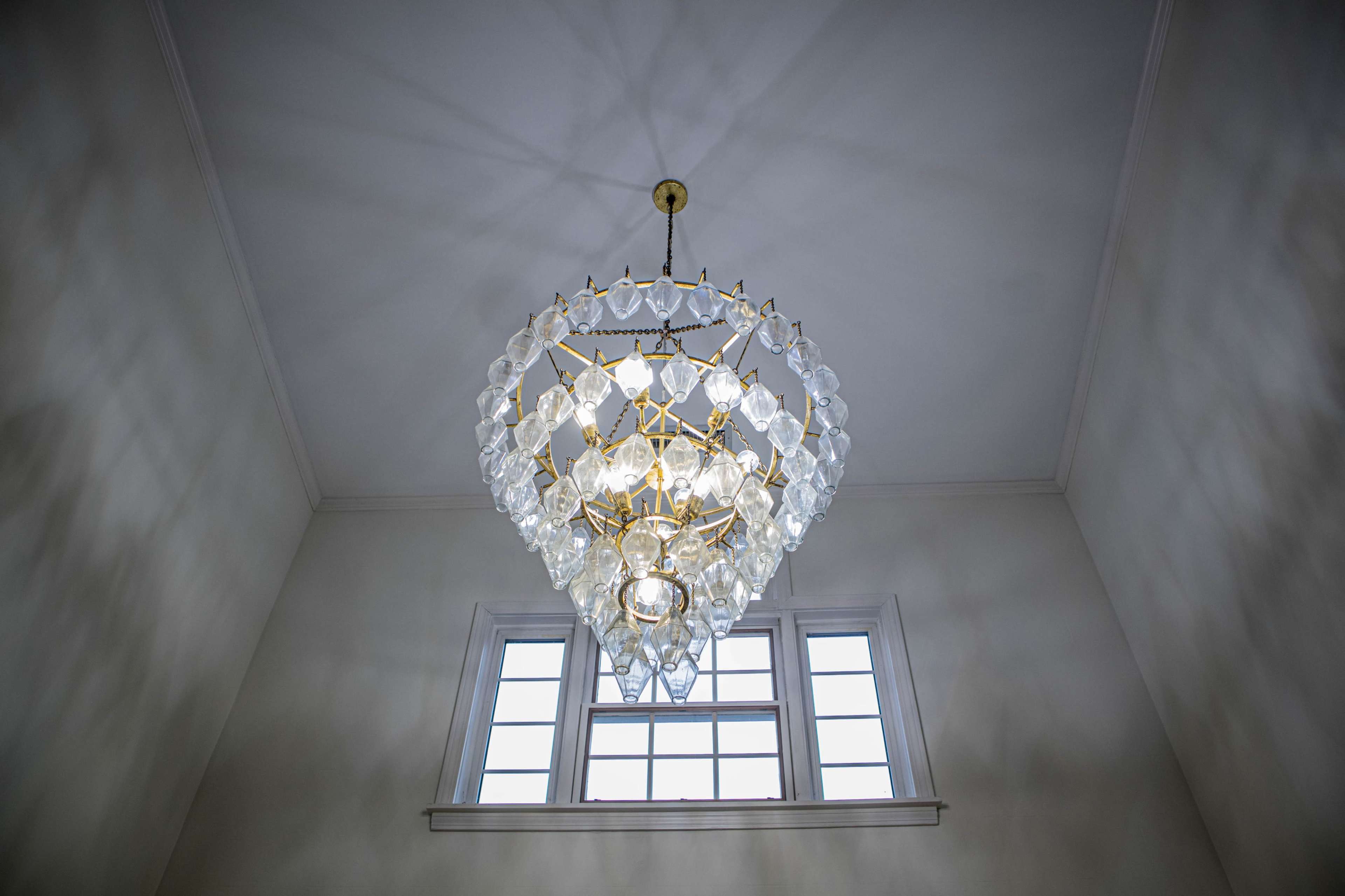 A large chandelier hangs from the ceiling, casting light and shadows on the walls beneath a set of windows.