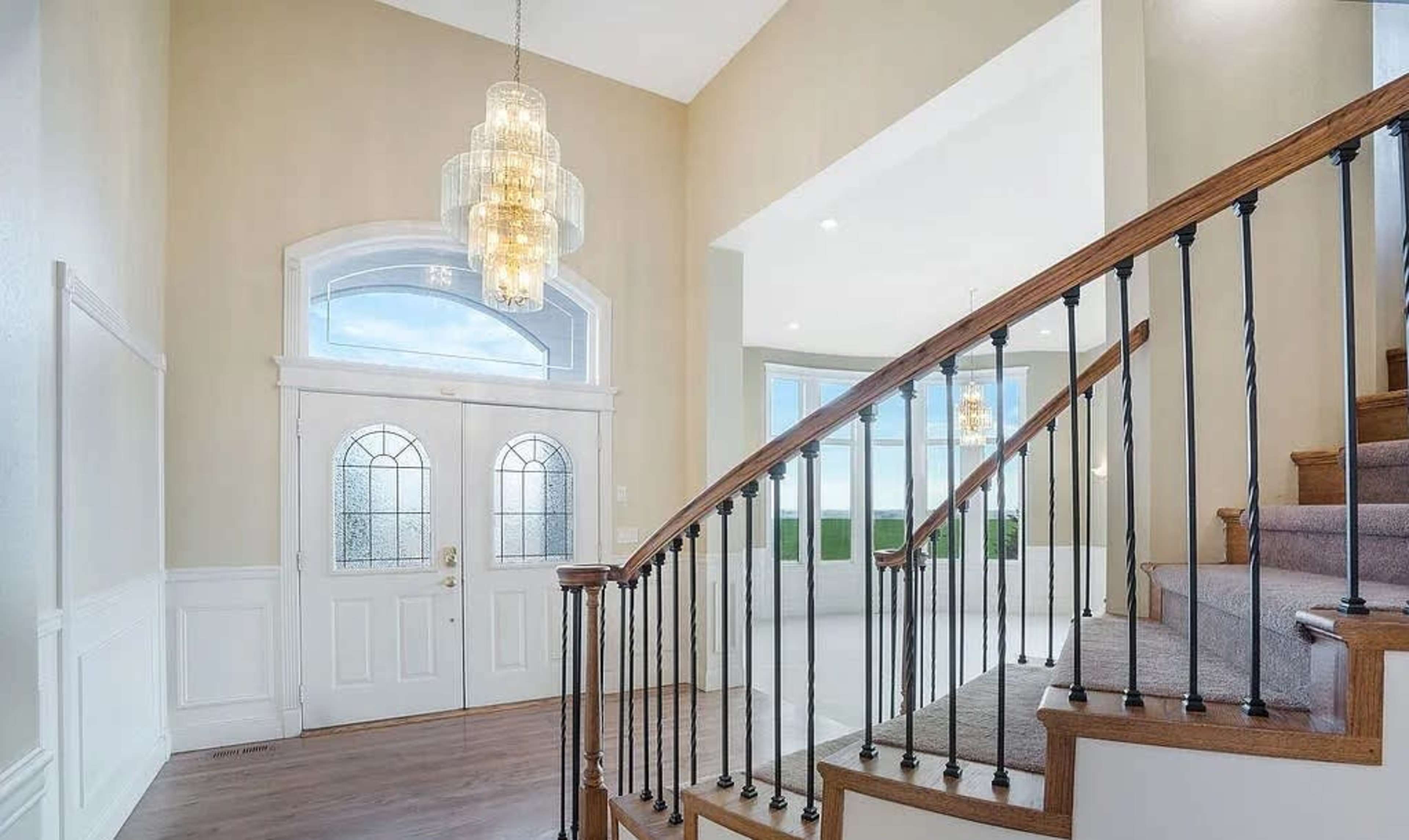 A spacious entryway with a curved staircase, a large chandelier, and double front doors.