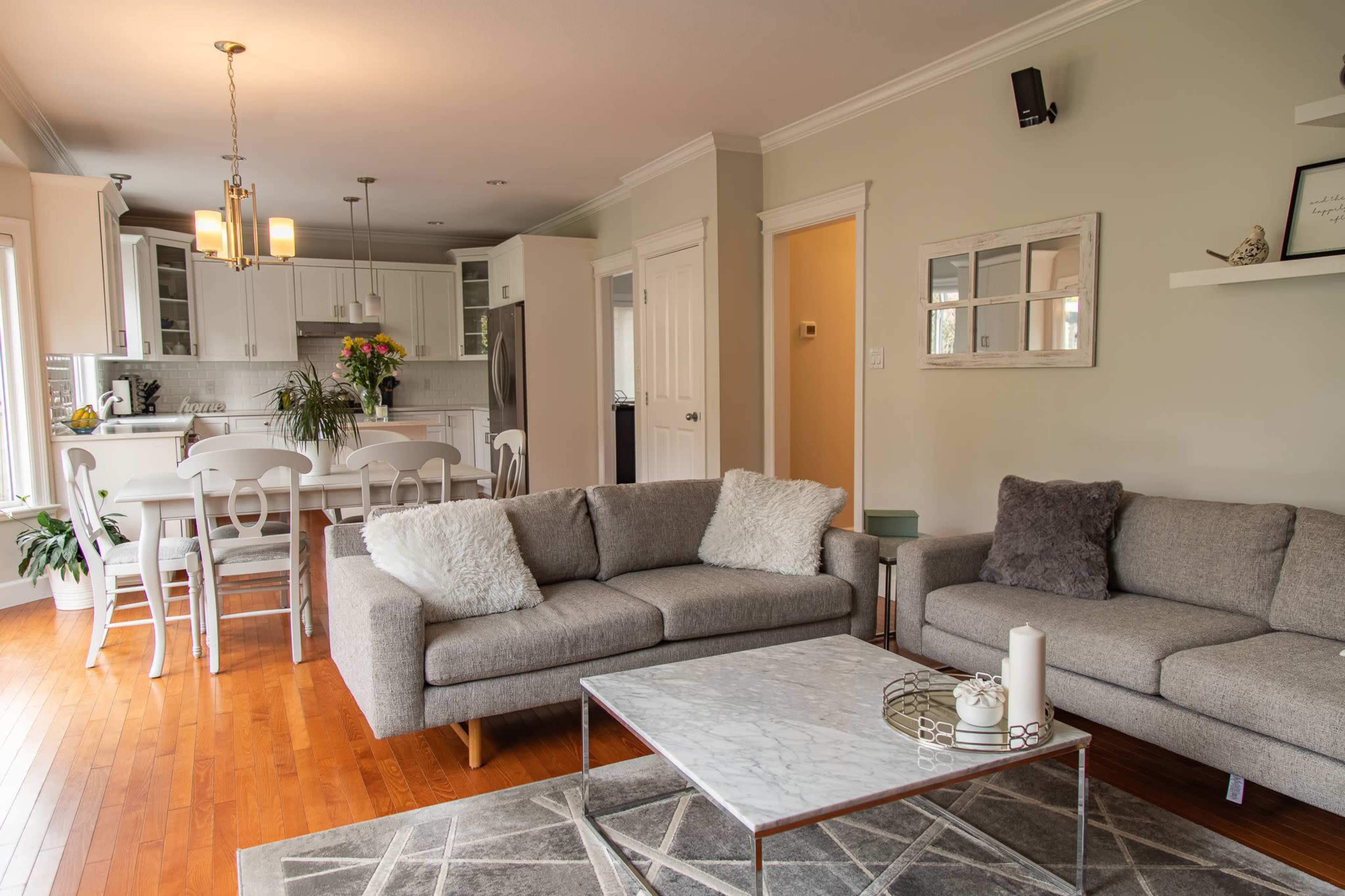 A modern living room with a gray sectional sofa, a marble-topped coffee table, and a view of a kitchen and dining area in the background.