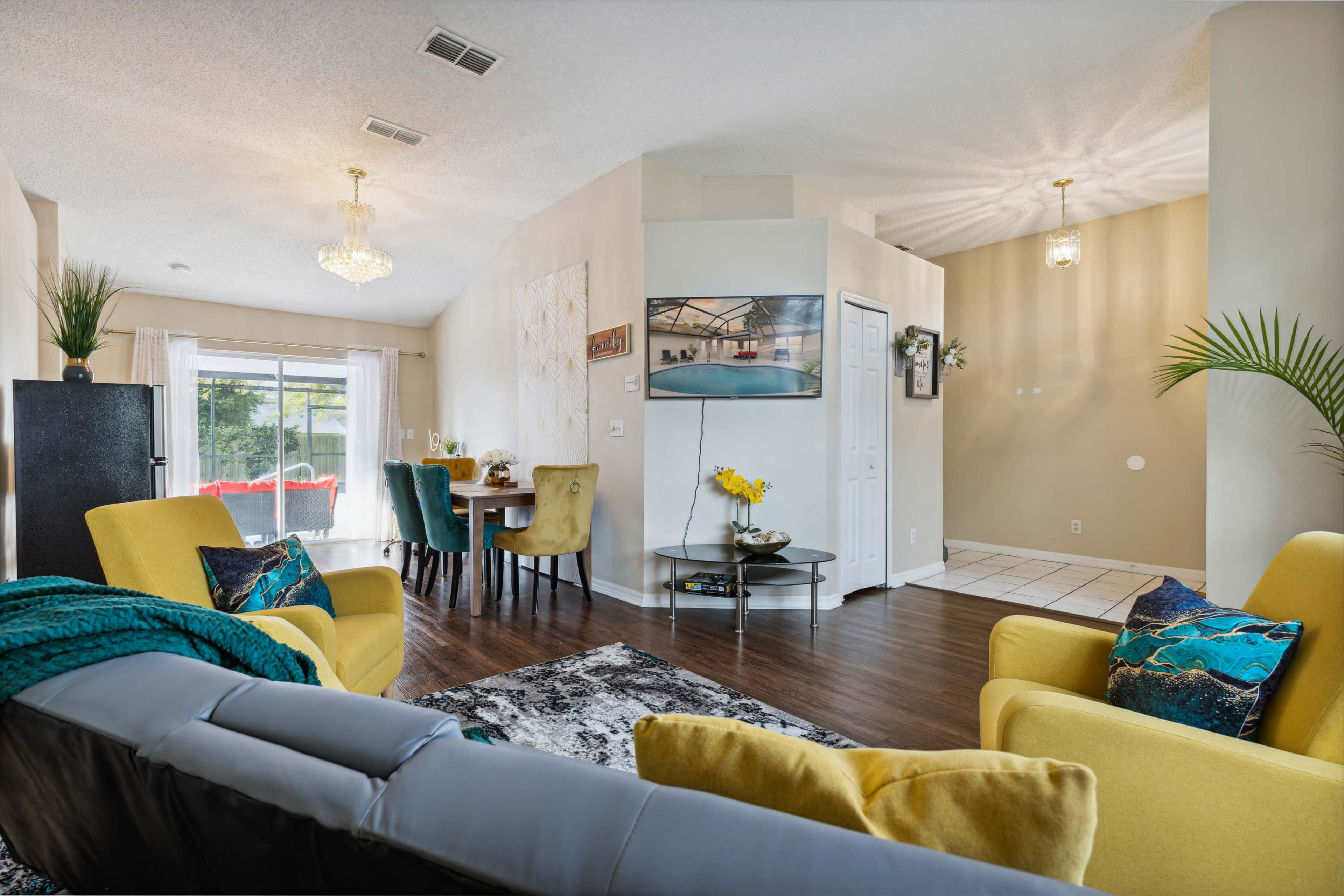 A bright living space featuring yellow and gray sofas, a dining area with chairs, and large windows that allow natural light to enter.