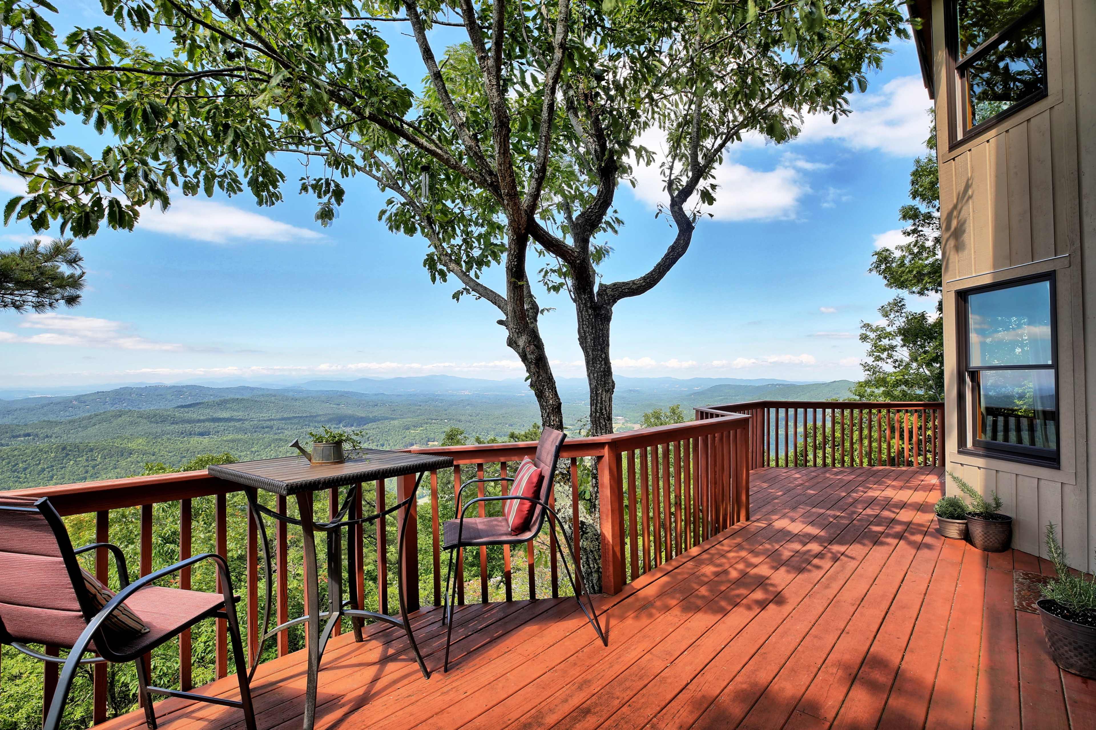 A wooden deck overlooking a mountainous landscape with a table and chairs near a tree.