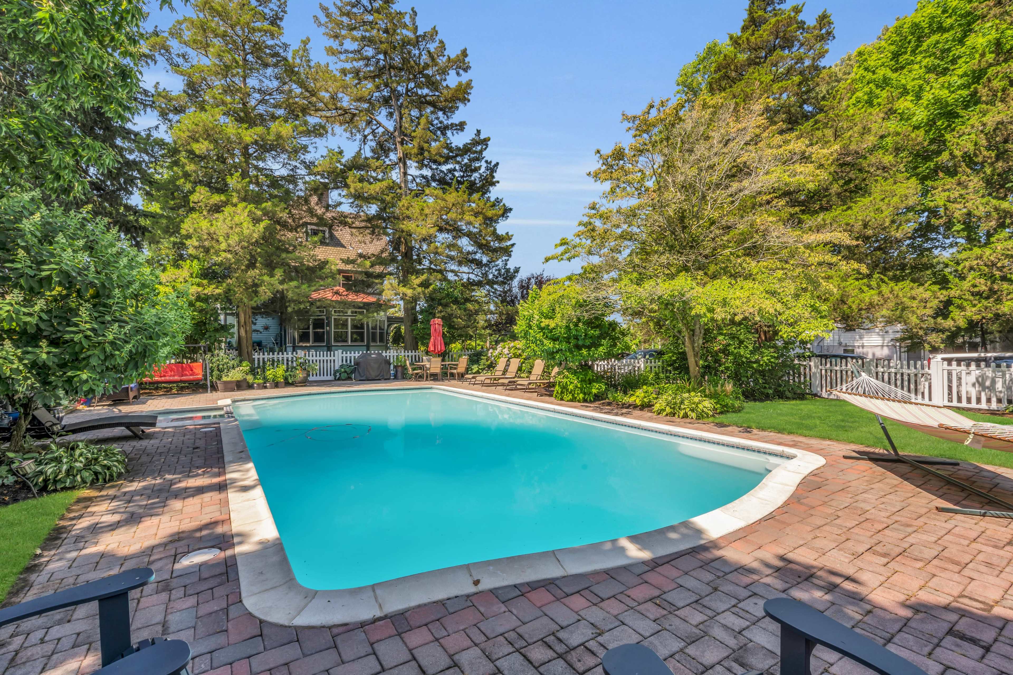 A residential backyard with a swimming pool surrounded by lounge chairs and lush greenery.