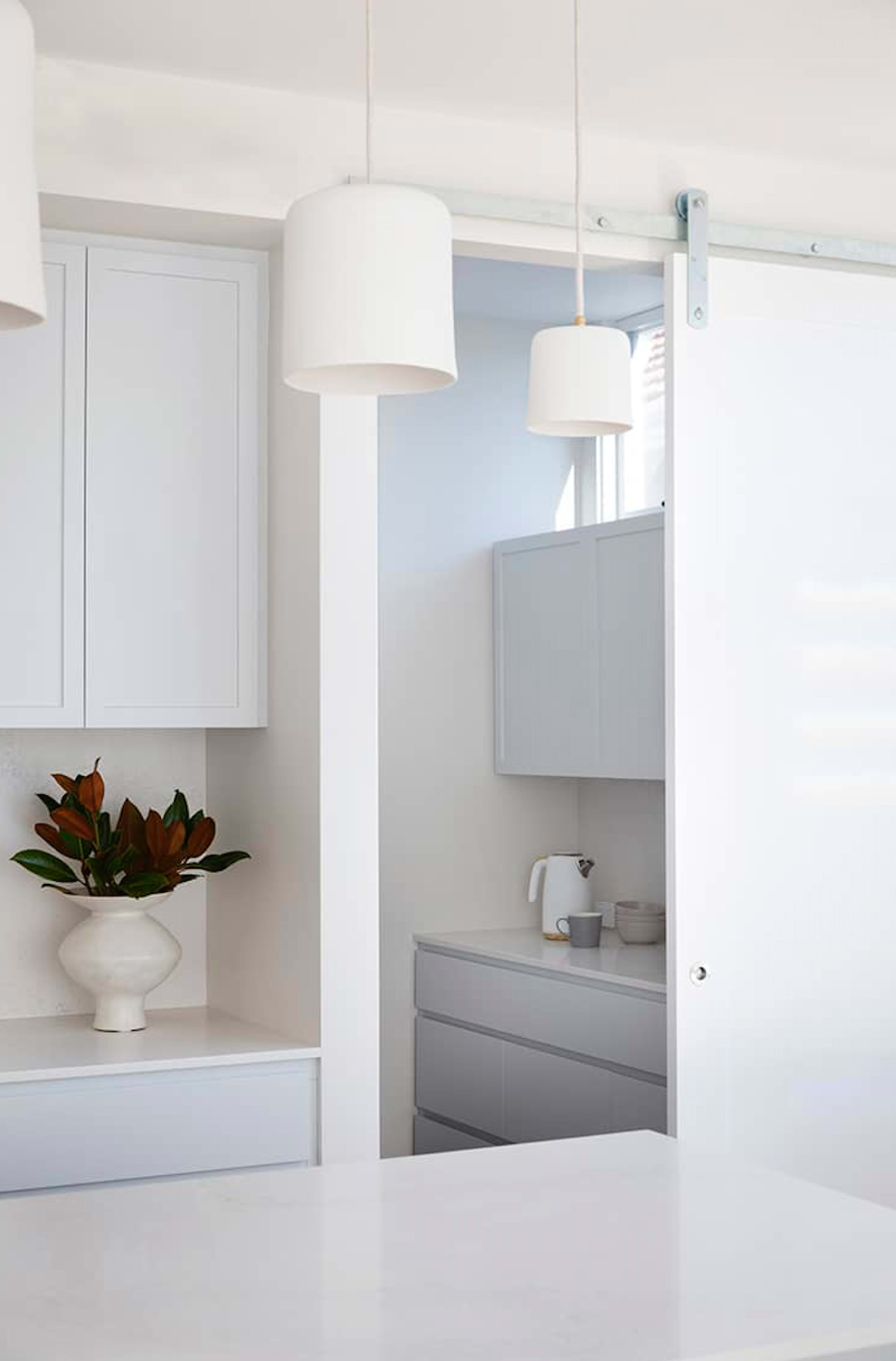 A modern kitchen with white cabinetry, a sliding door, and a small part of another room visible through the door.