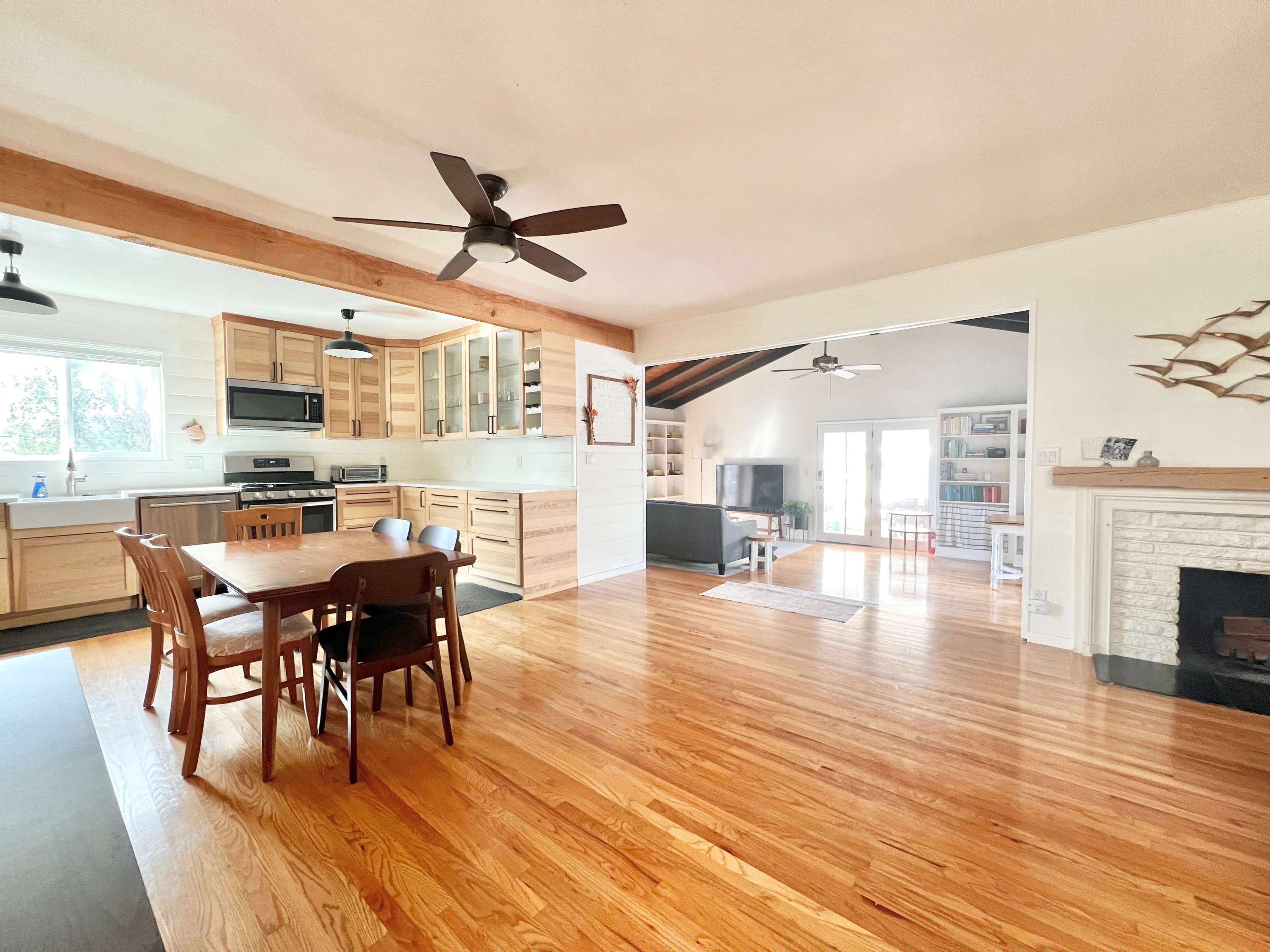The image shows a spacious kitchen and dining area with wooden floors, a dining table, and an open layout leading to a living room.