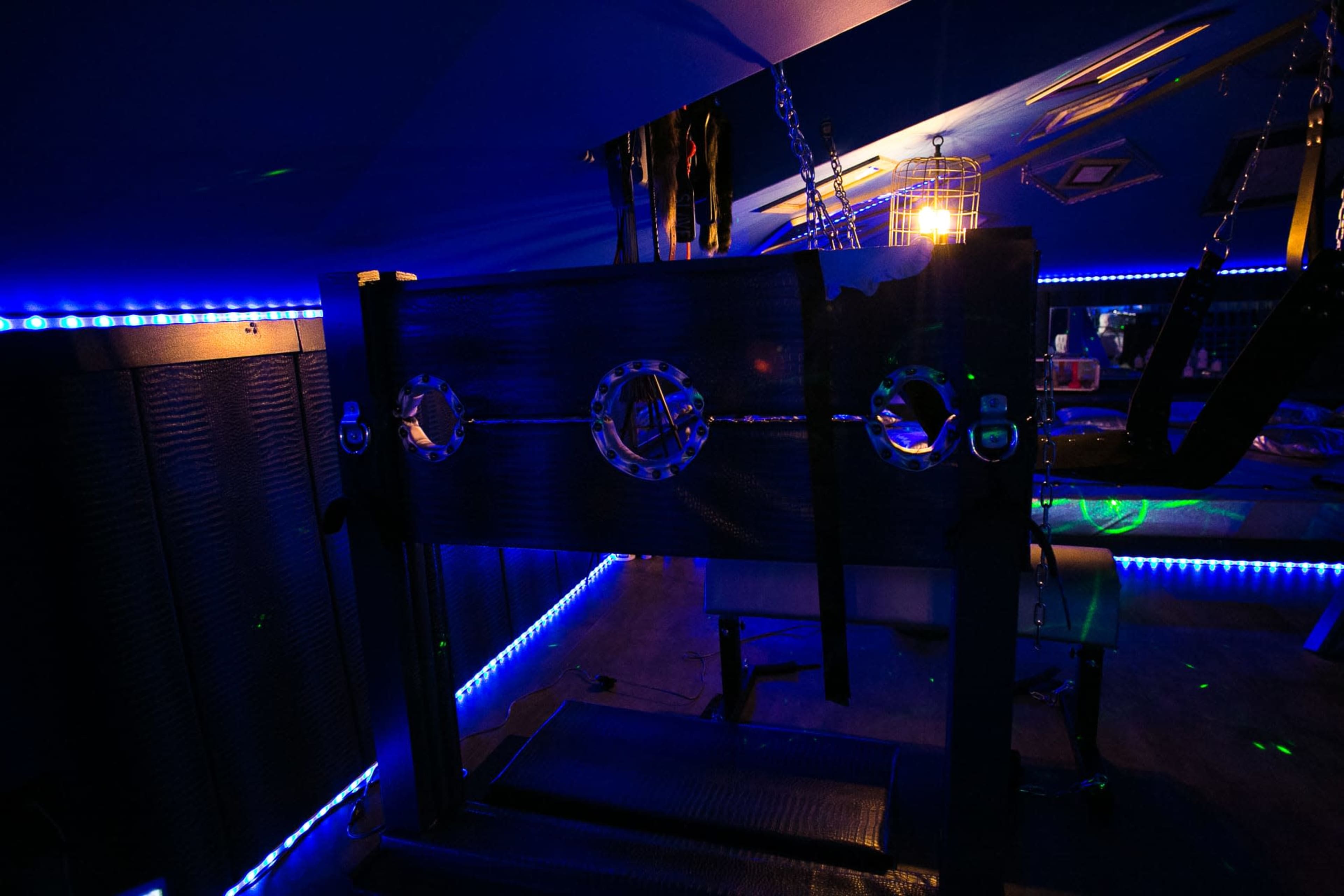 A dimly lit room featuring a stocks mechanism against a backdrop of blue LED lighting and various accessories hanging from the ceiling.
