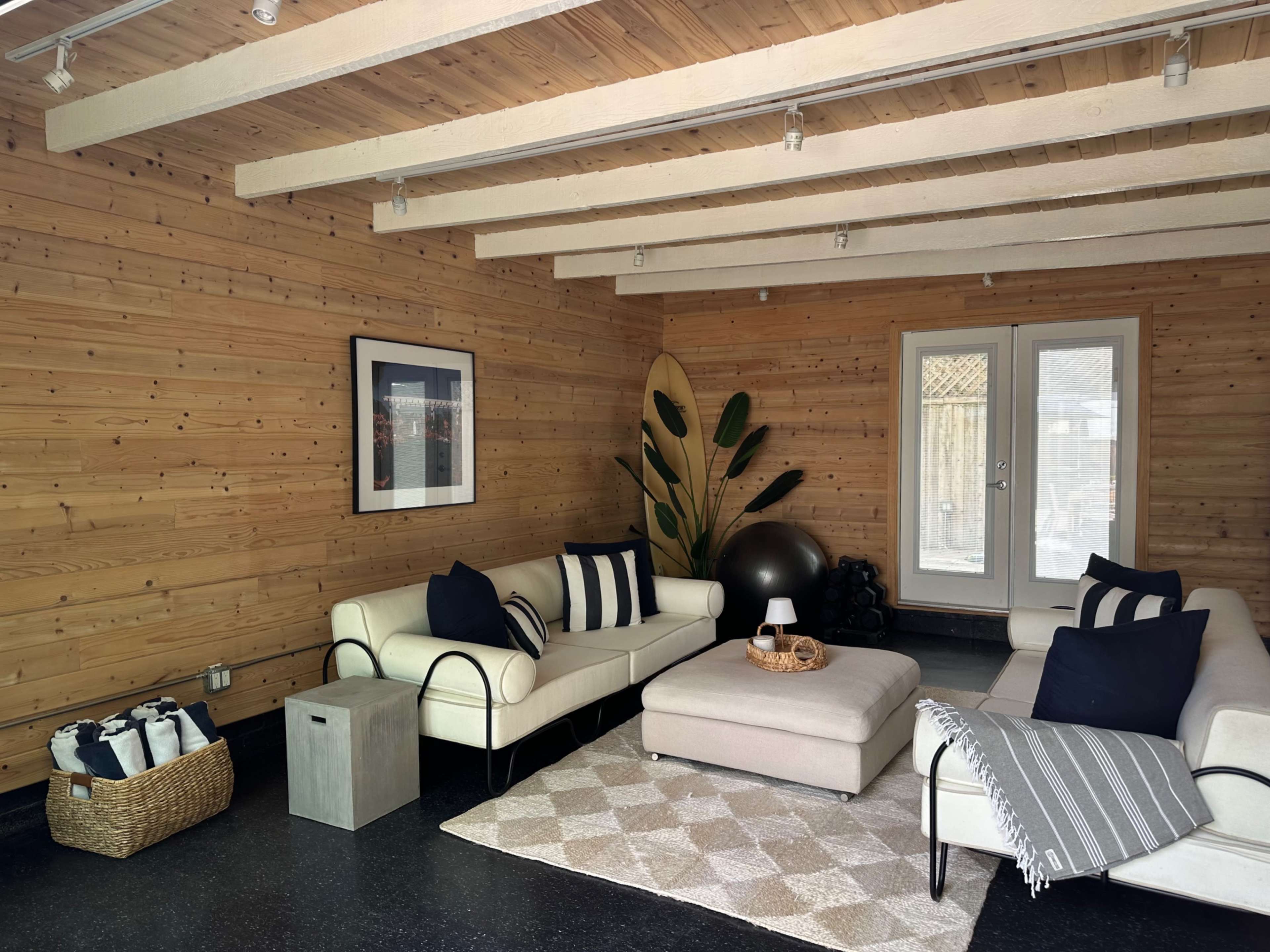 The image shows a modern living room with a wood-paneled wall, two couches, a coffee table, and large windows.