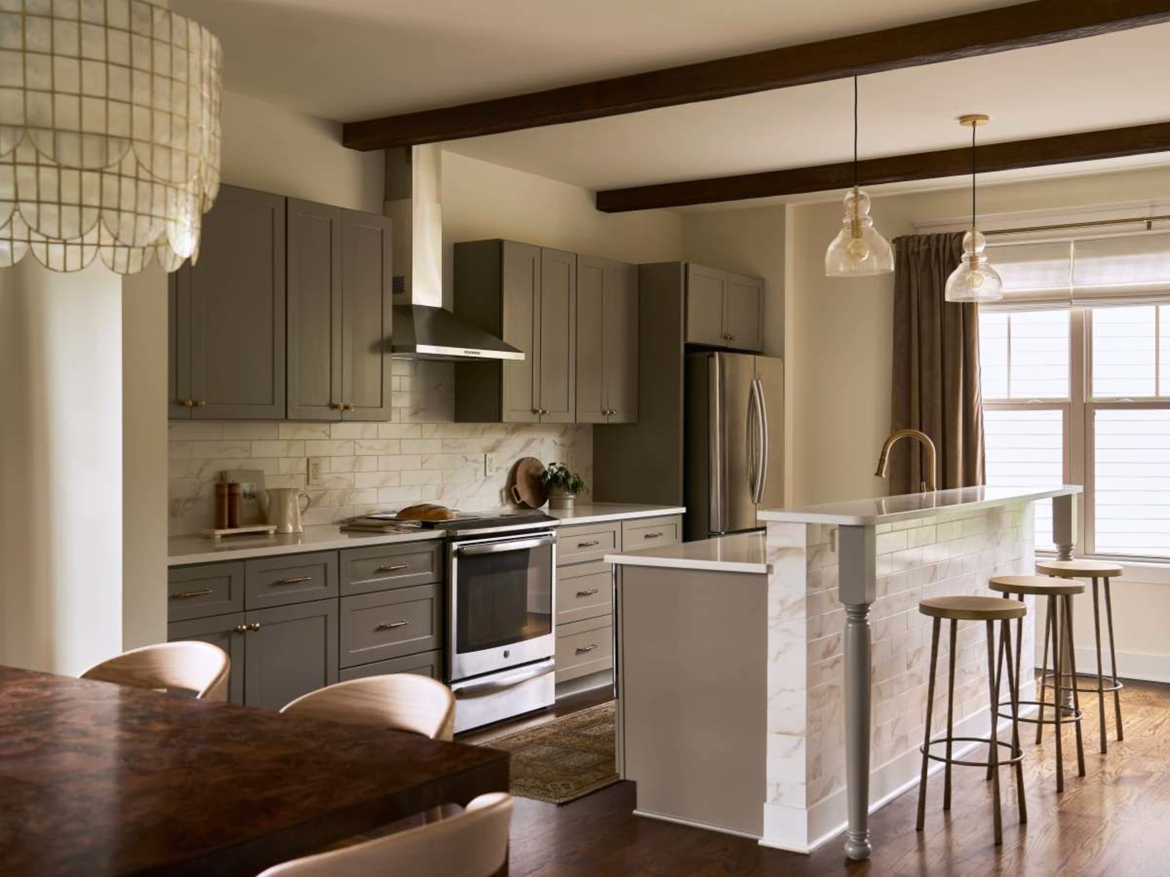 The kitchen features gray cabinetry, modern stainless steel appliances, and a dining area with wooden accents and bar stools.