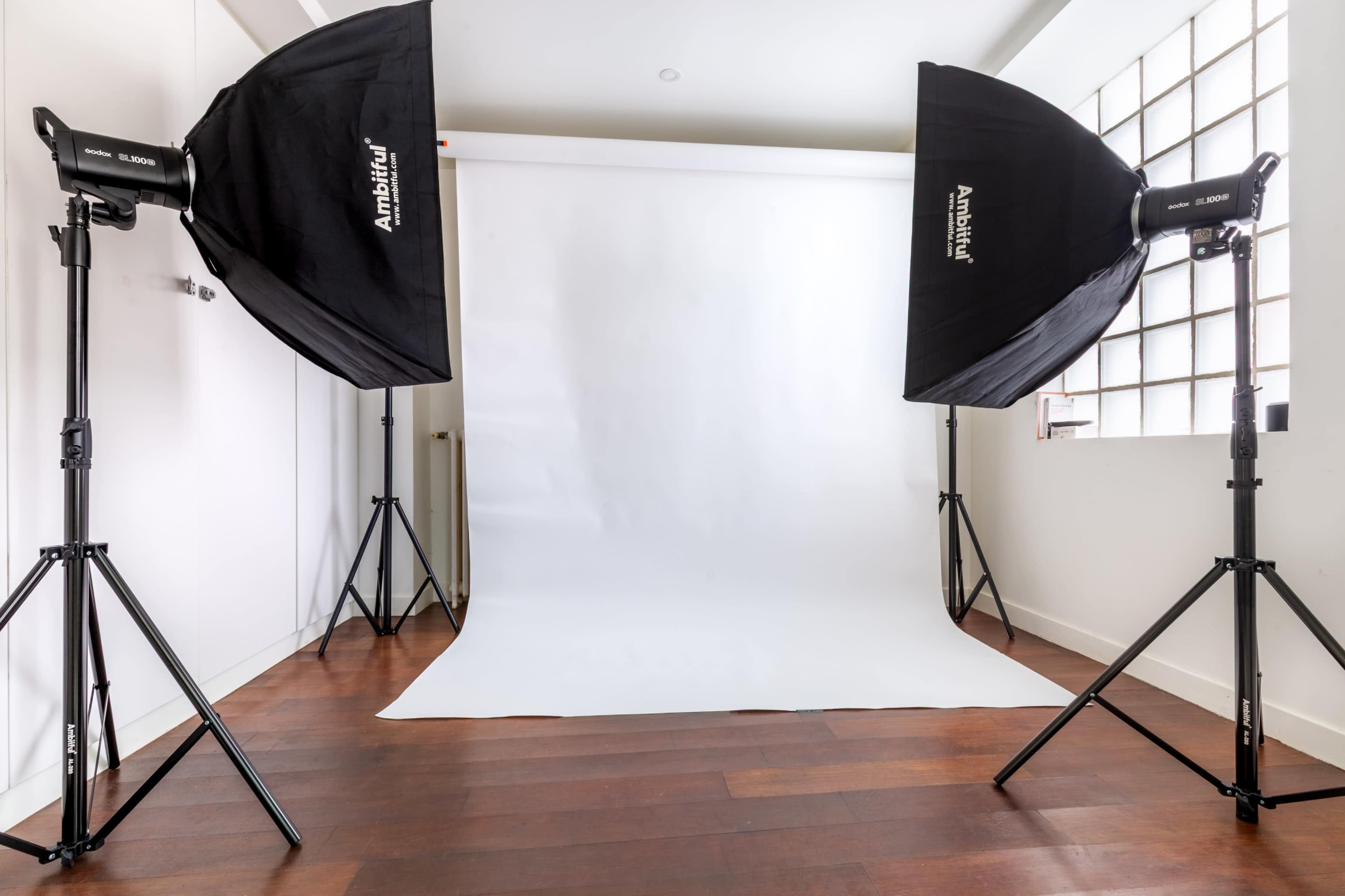 The image shows a photography studio setup with a white backdrop and two softbox lights positioned on either side.