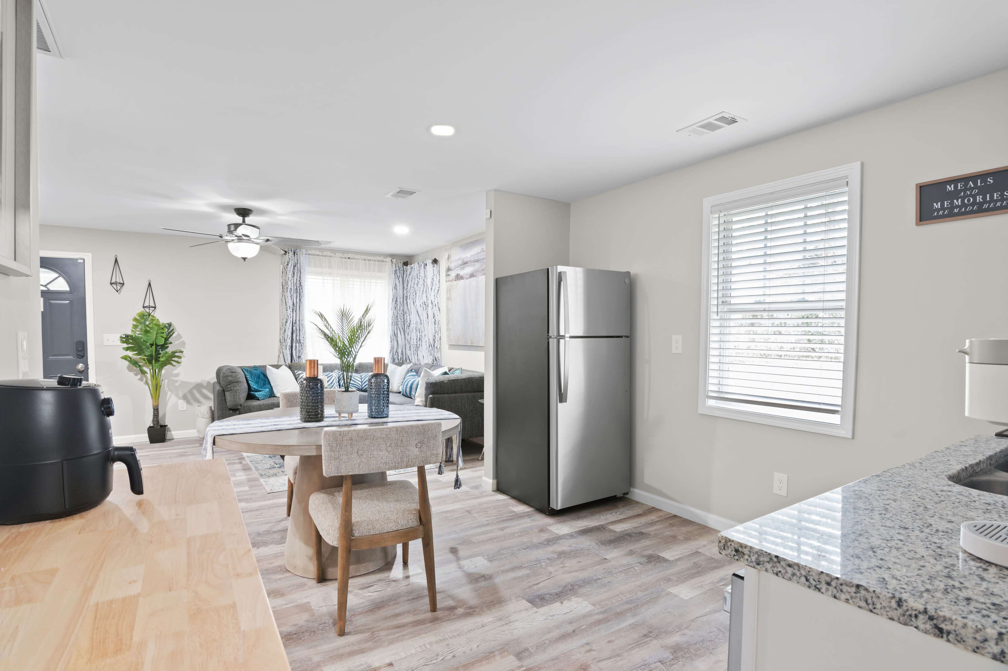 The image shows a modern kitchen and living area with a round dining table, a refrigerator, and a cozy seating arrangement with a sofa.