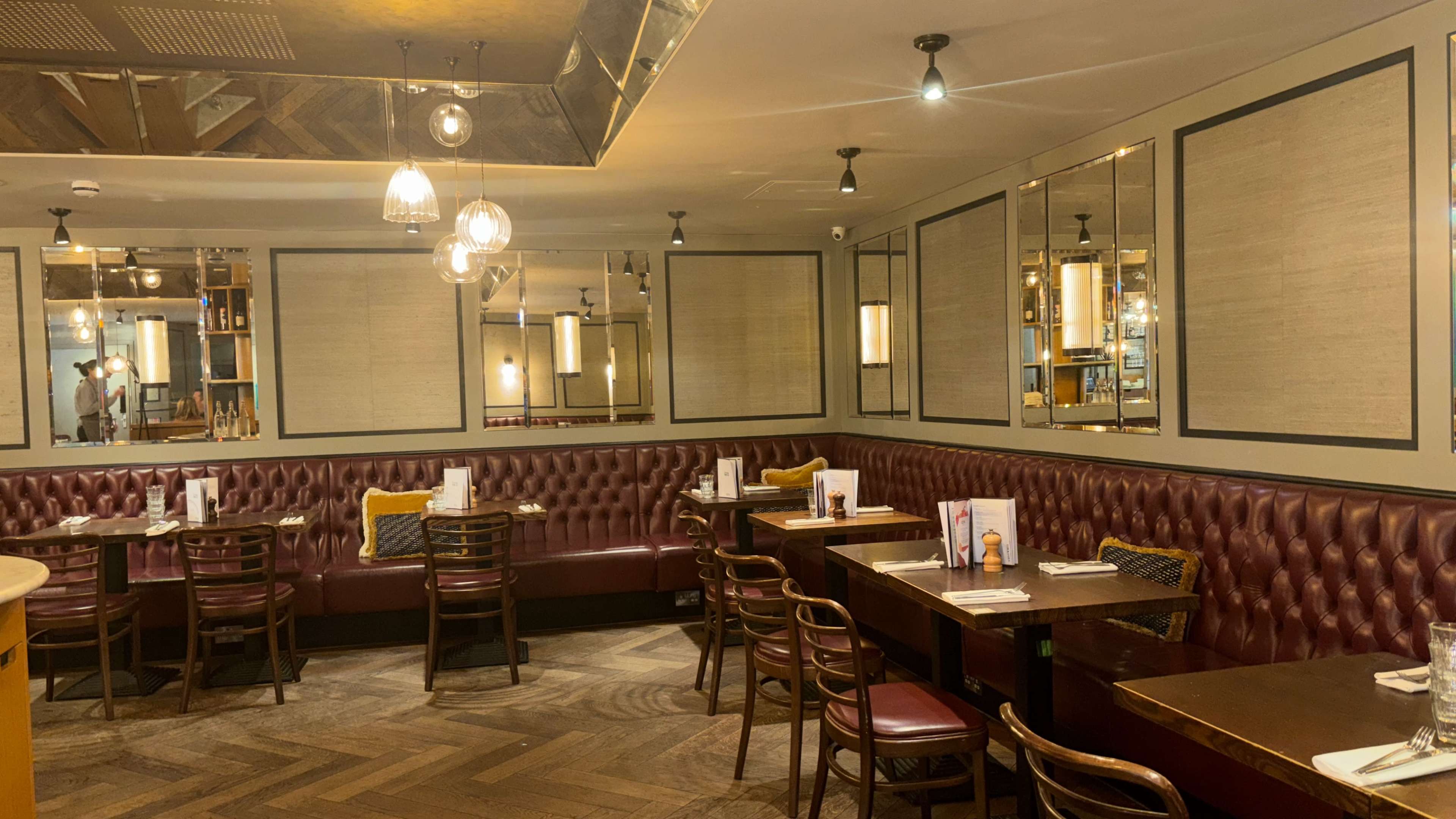 The image shows a cozy restaurant interior with wooden flooring, leather tufted seating, and tables set for dining.