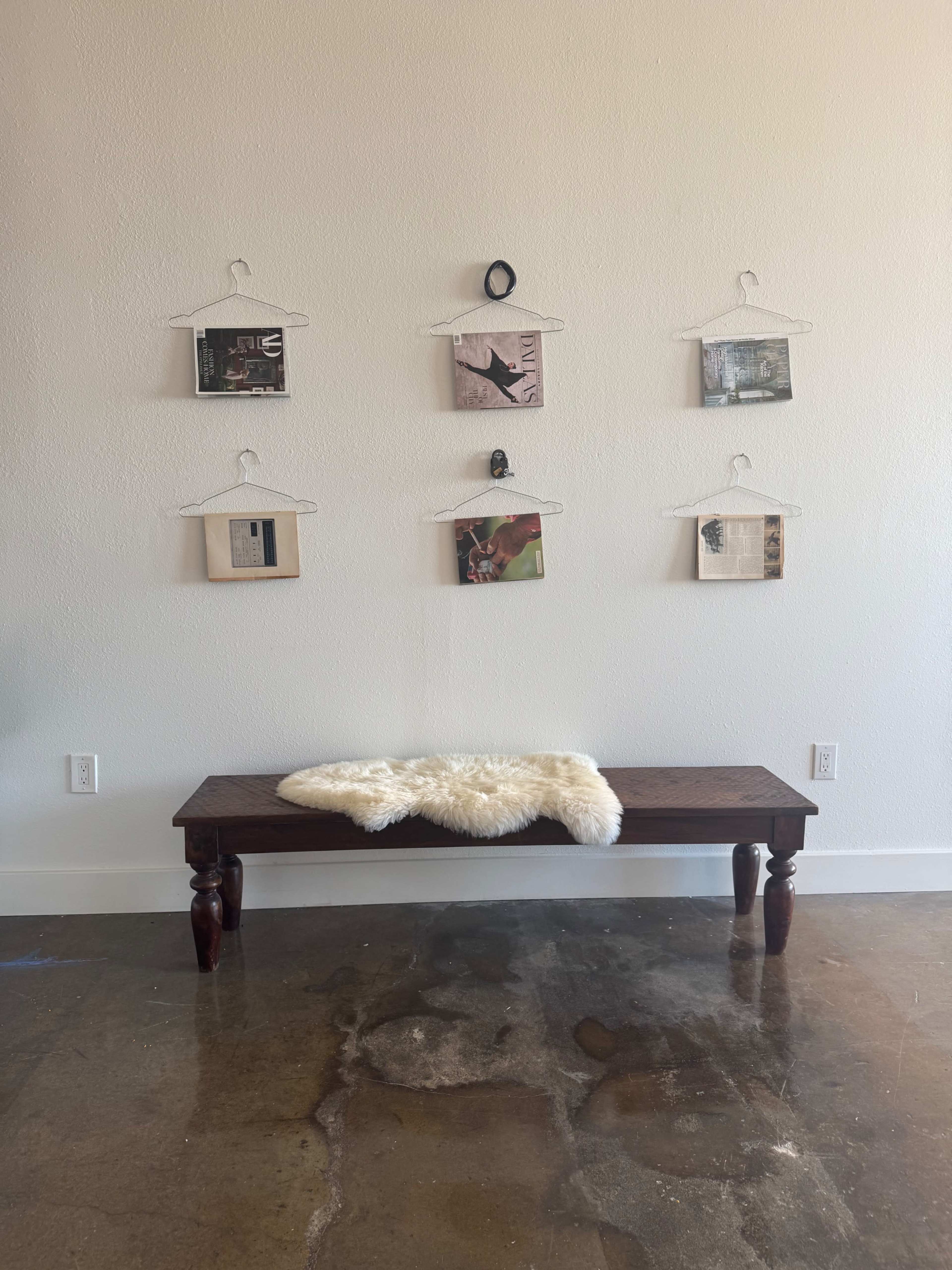 A wooden bench with a fur throw sits in front of a wall adorned with six framed artworks hanging from plastic clips.