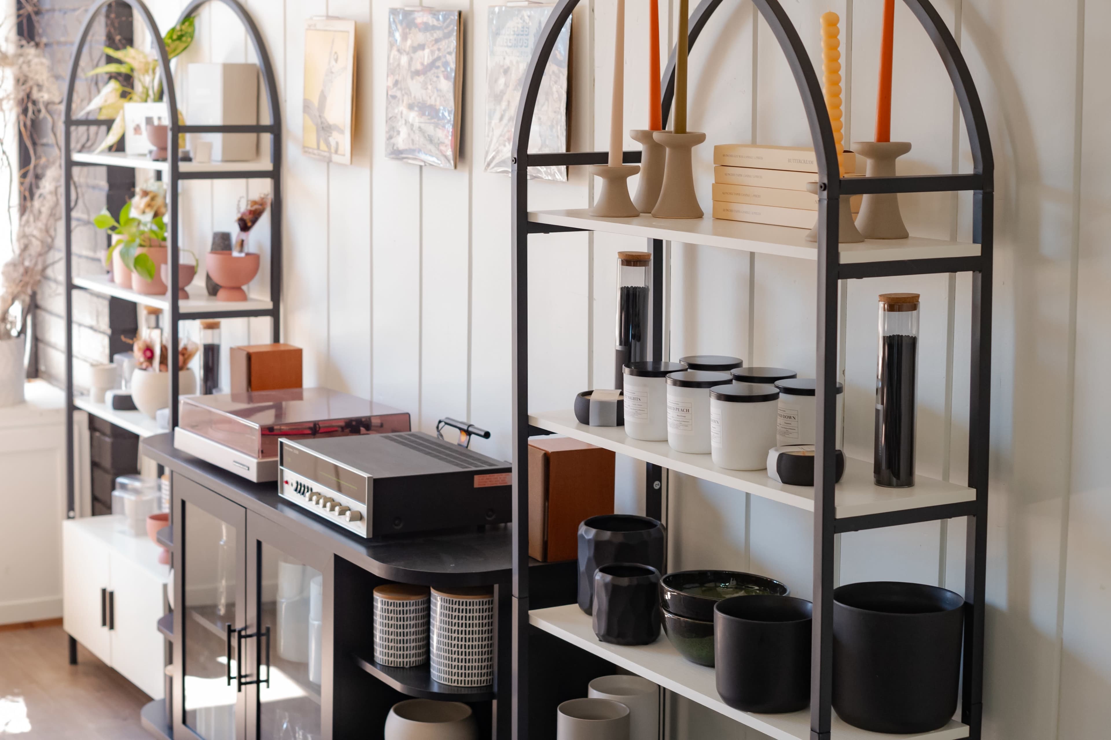 The image depicts a modern interior with open shelving units displaying various decorative items, plants, and a record player.