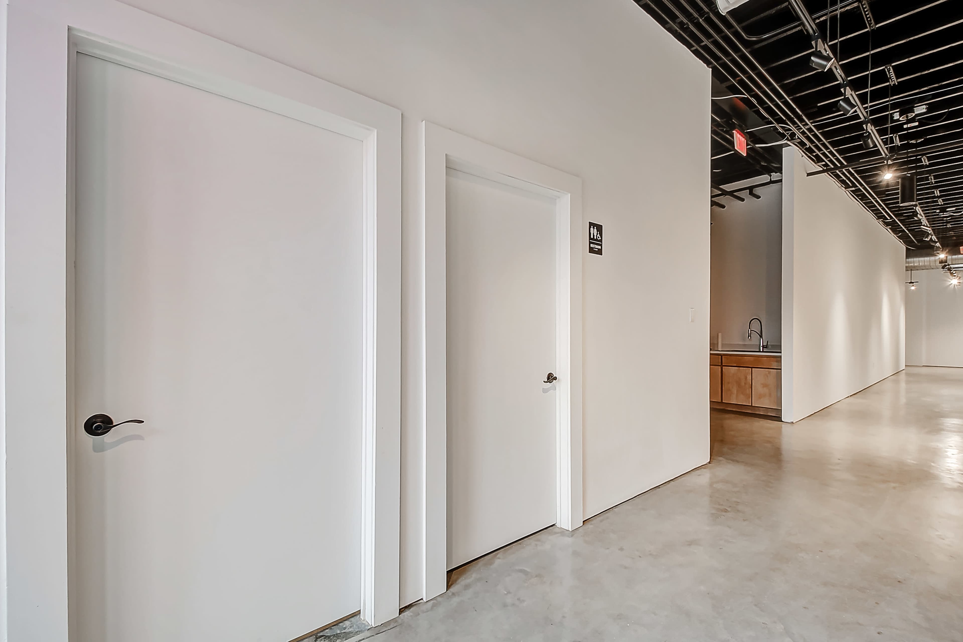 A clean corridor features two white doors on the left, leading to separate rooms, while a kitchen area is visible in the background.