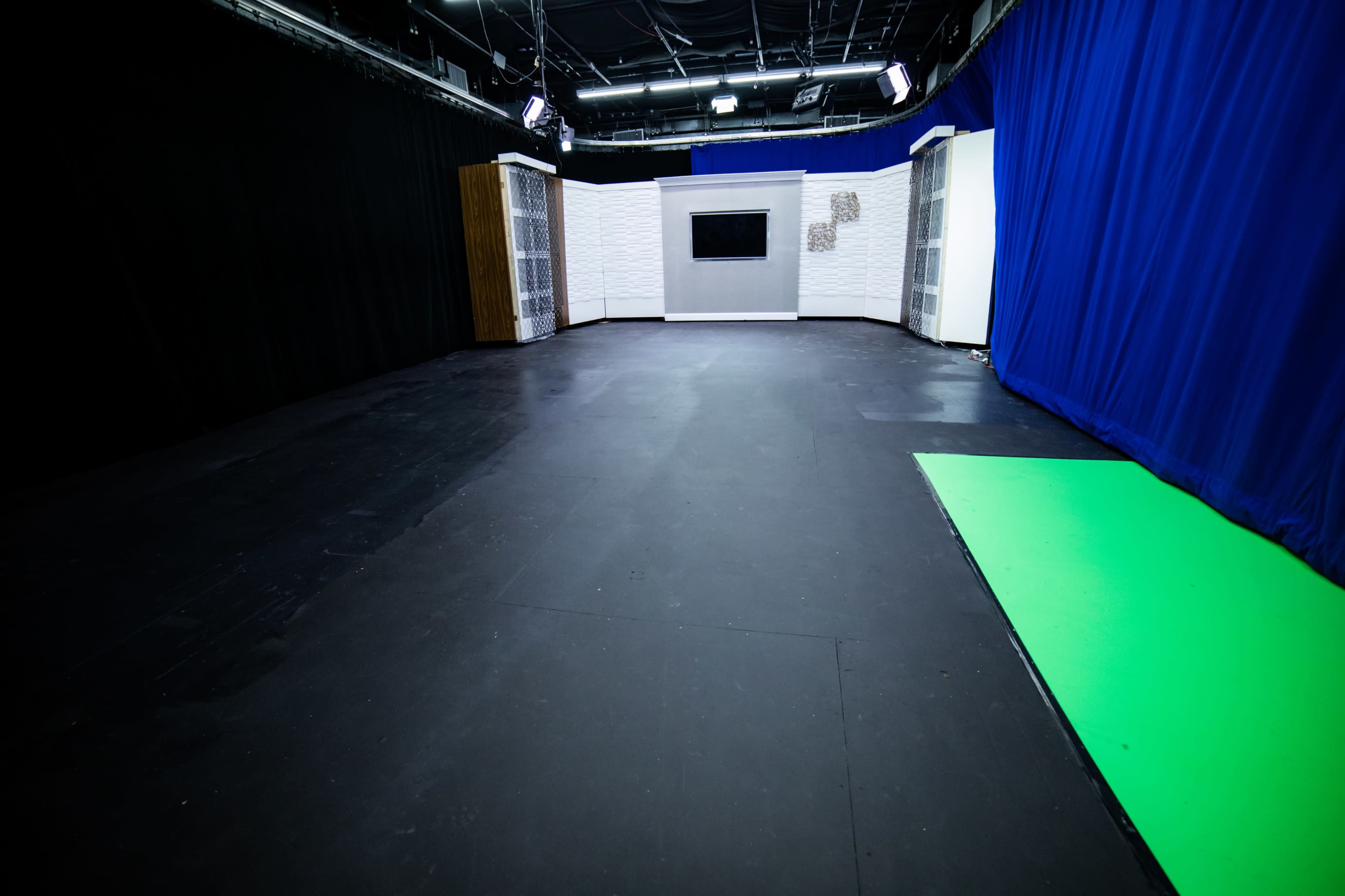 The image shows a television studio with a green screen area, a gray backdrop, and shelves on either side of the space.