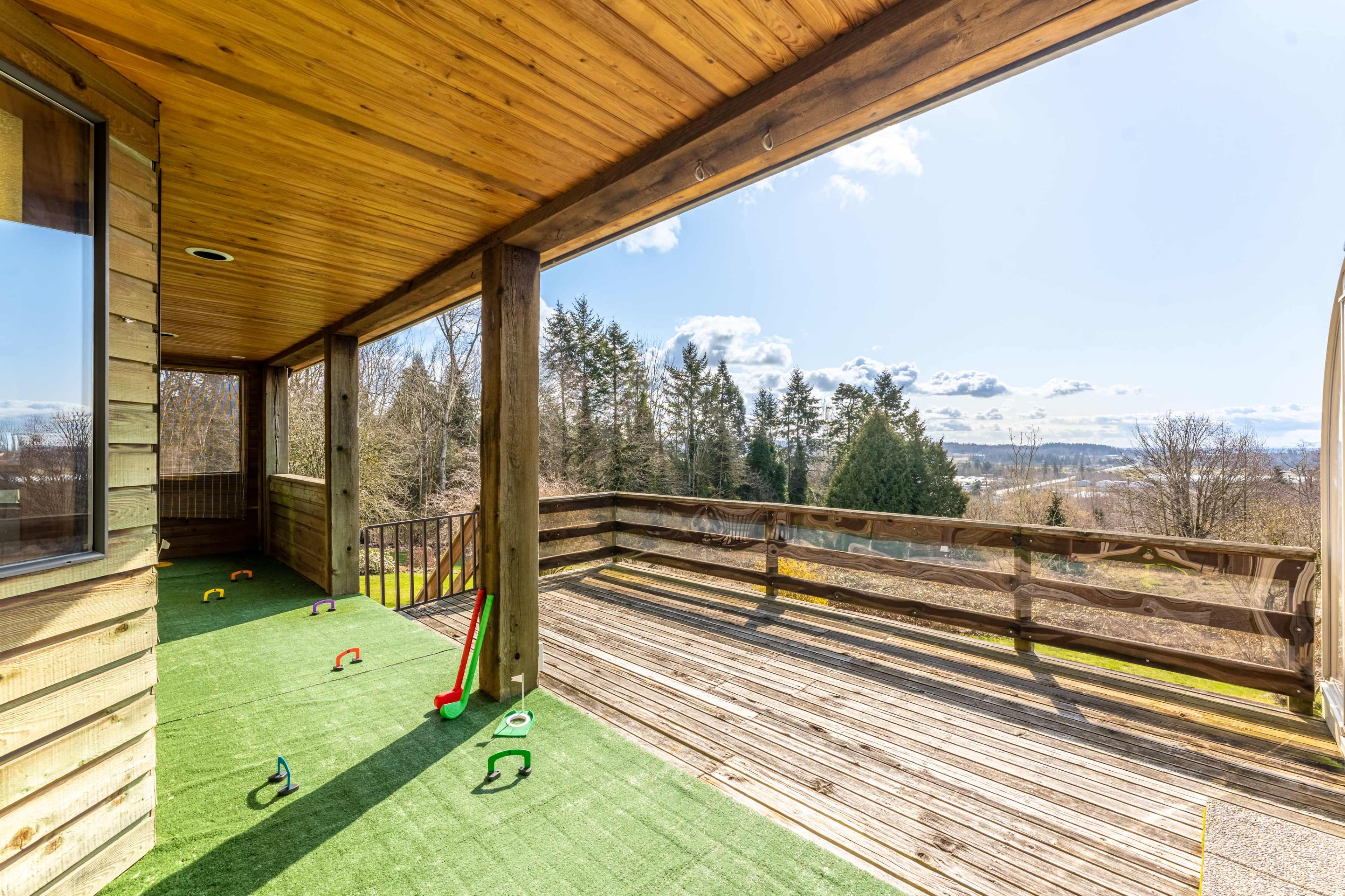 A wooden deck with artificial grass, overlooking a scenic landscape with trees and a distant view of hills under a clear sky.