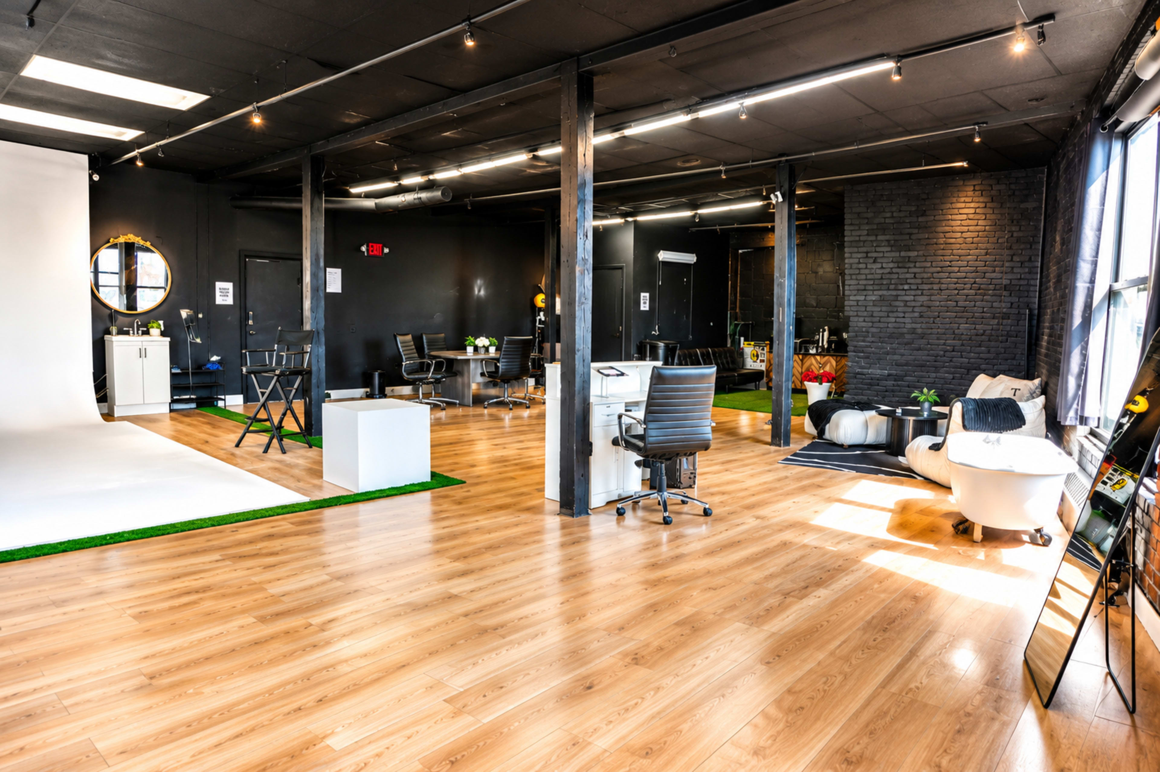 The image shows a spacious, modern office interior with wooden flooring, various workstations, and a photography backdrop in a well-lit environment.