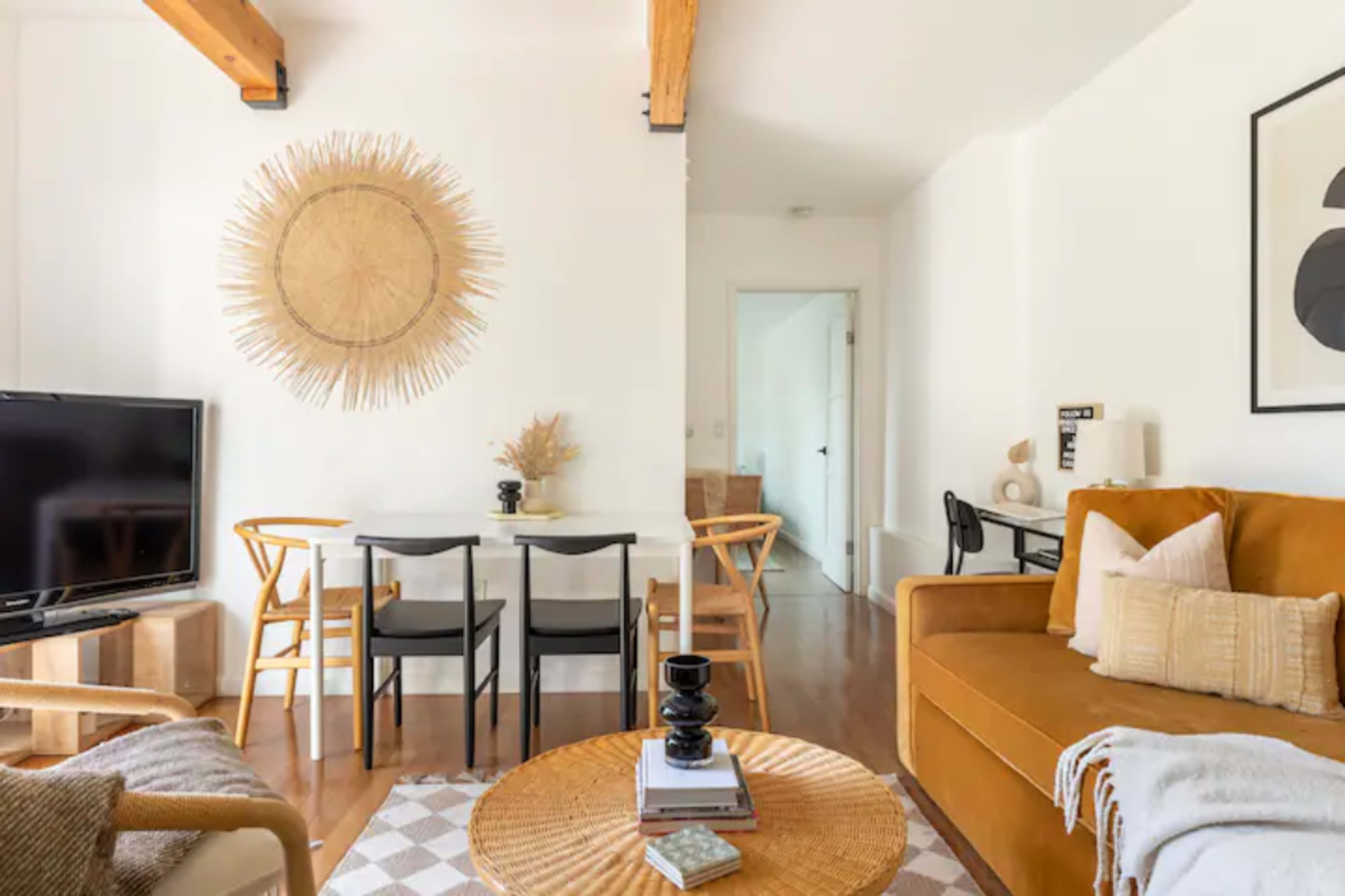 The image shows a modern living space with a cozy brown sofa, a round coffee table, a dining area with a black table and chairs, and decorative wall elements.