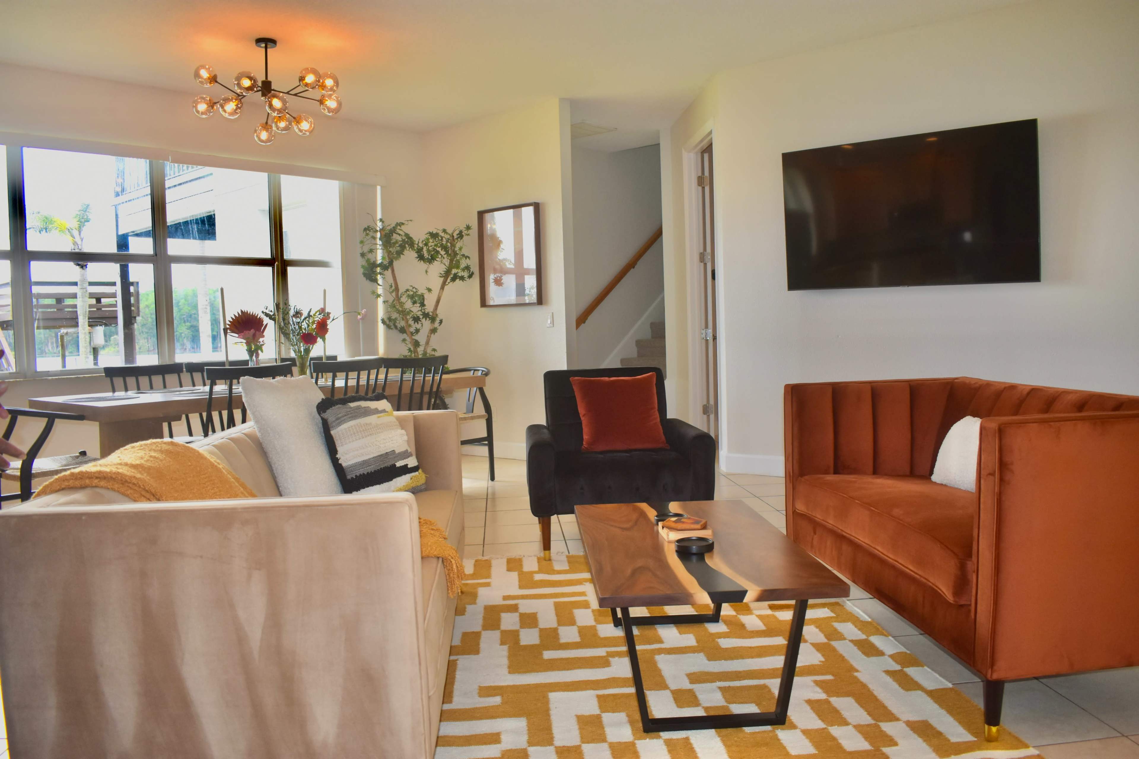 A modern living room featuring two sofas, a coffee table, and a television on the wall, with a dining area visible in the background.