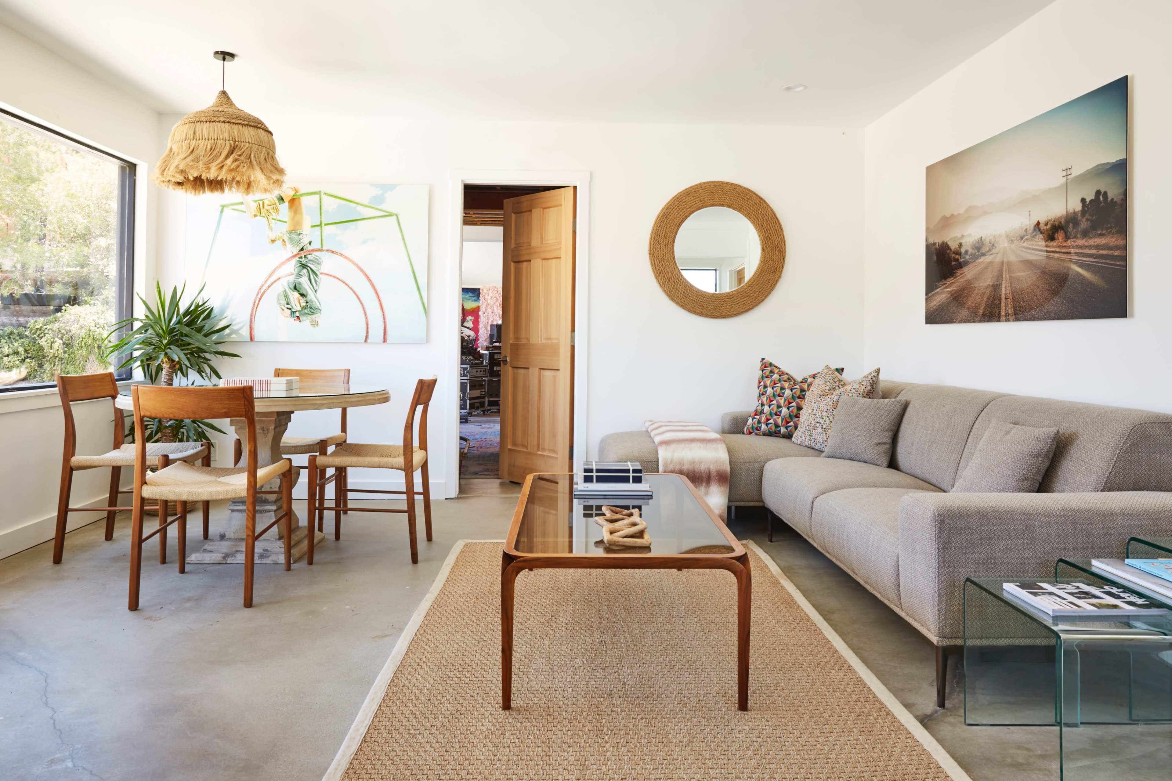 A modern living room and dining area with a neutral color palette, featuring a sofa, a wooden dining table, and decorative wall art.