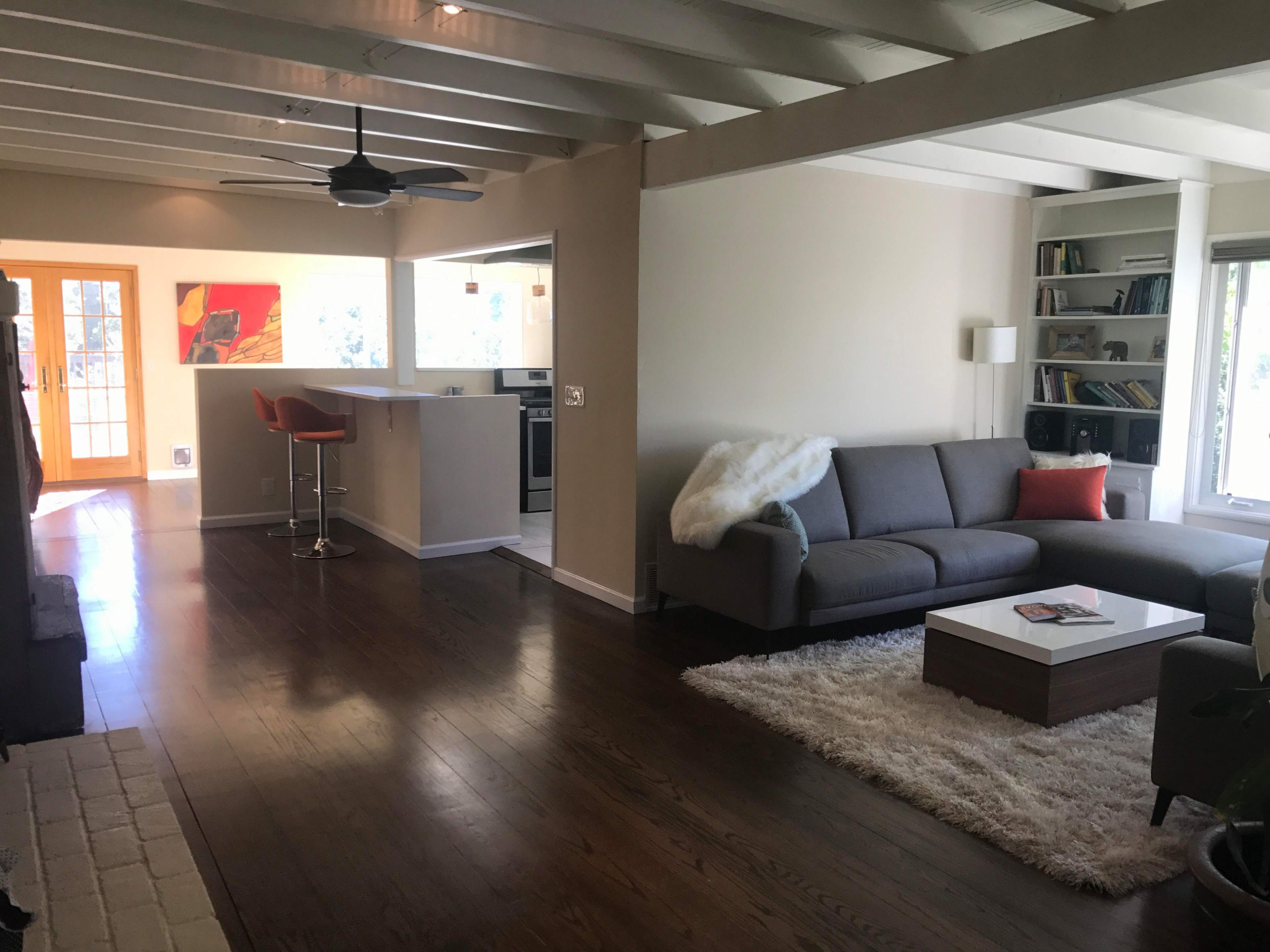 A spacious living room features a gray sofa, a coffee table on a plush rug, and a view of an open kitchen with bar seating.