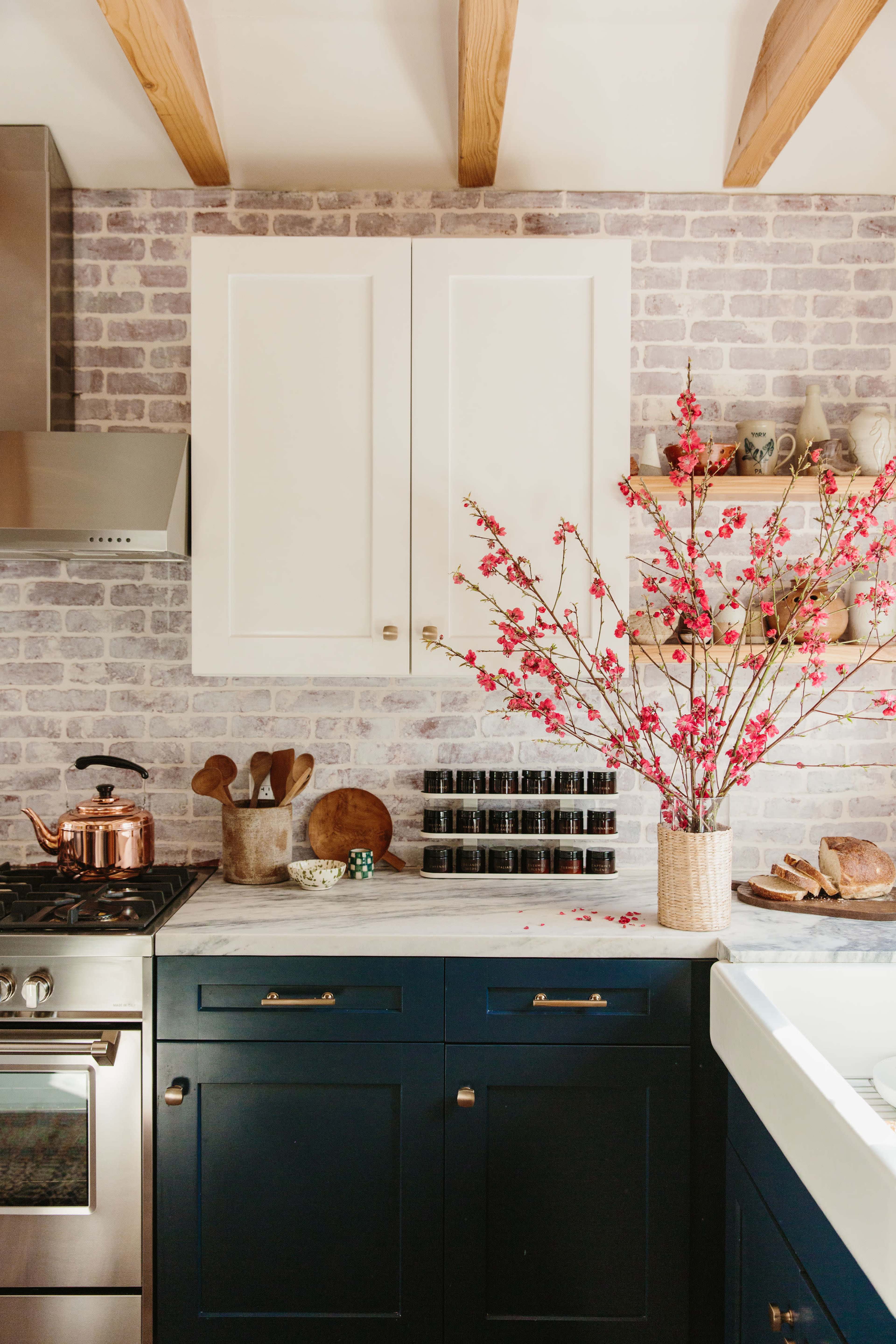 A kitchen with navy blue cabinets, a stainless steel stove, and a decorative arrangement of pink branches in a vase sits on a countertop.