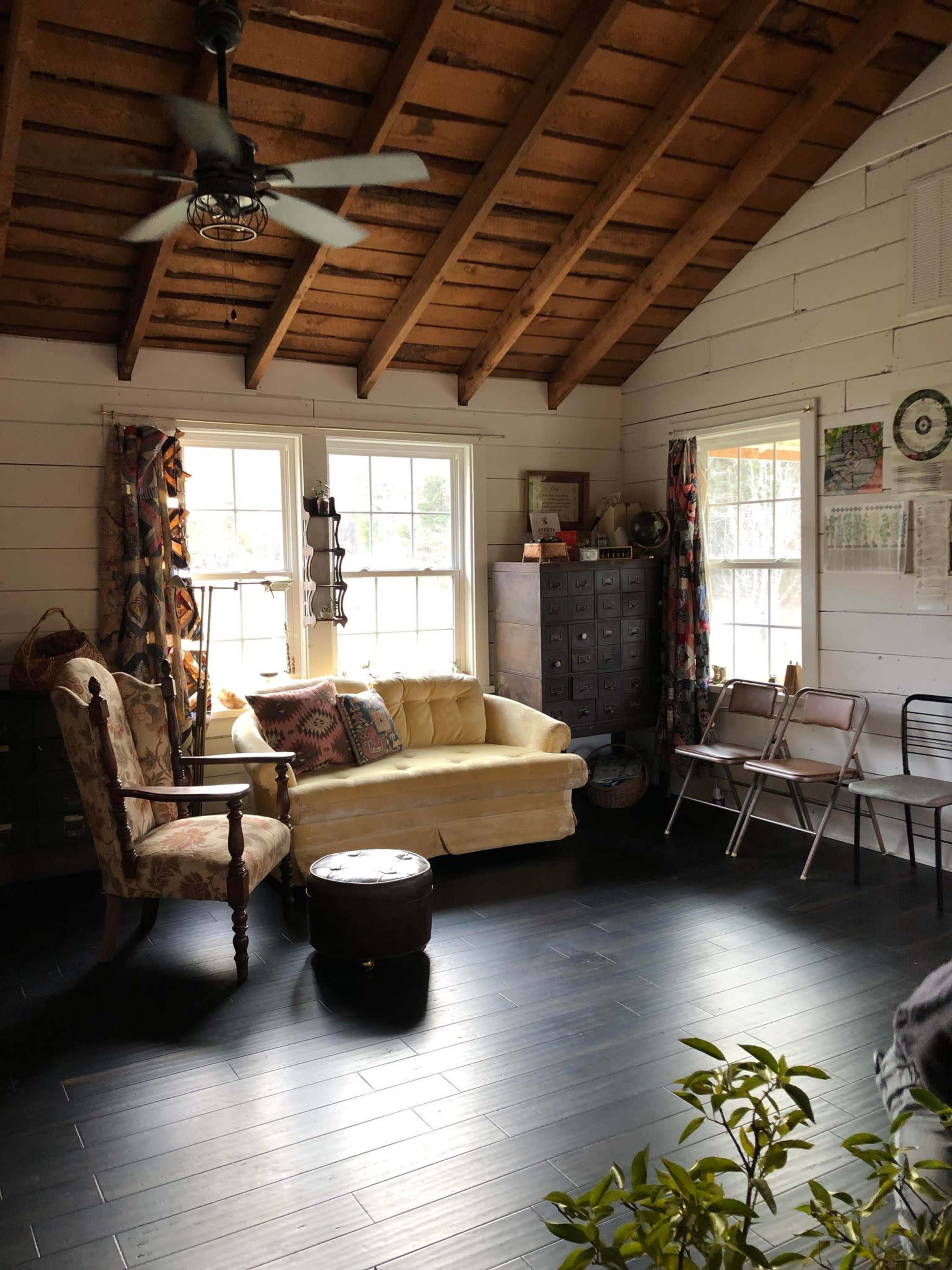The living room features a yellow couch, a decorative armchair, and several windows with wooden beams overhead.