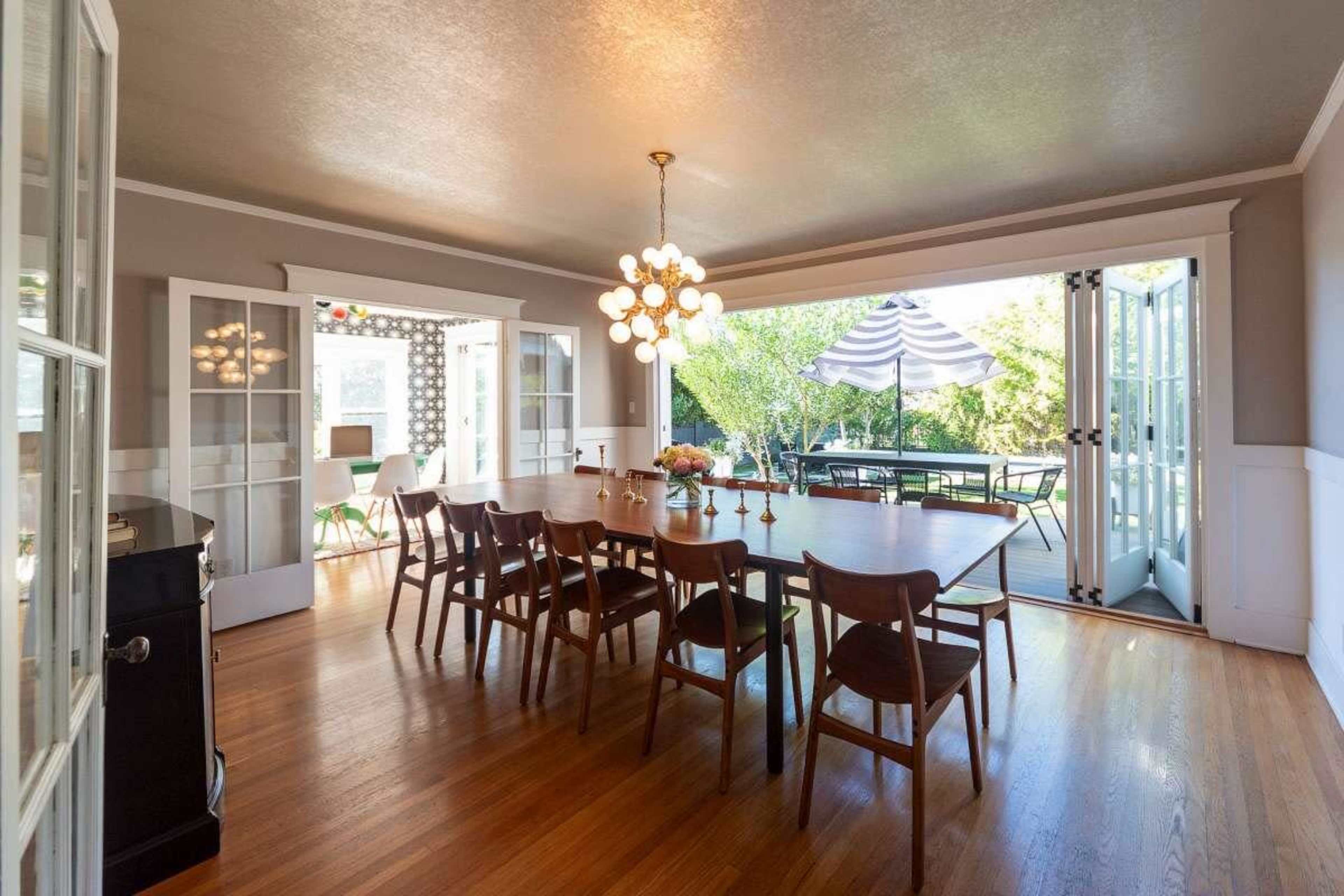 A spacious dining room features a long wooden table surrounded by chairs, with large glass doors that open to a patio area.