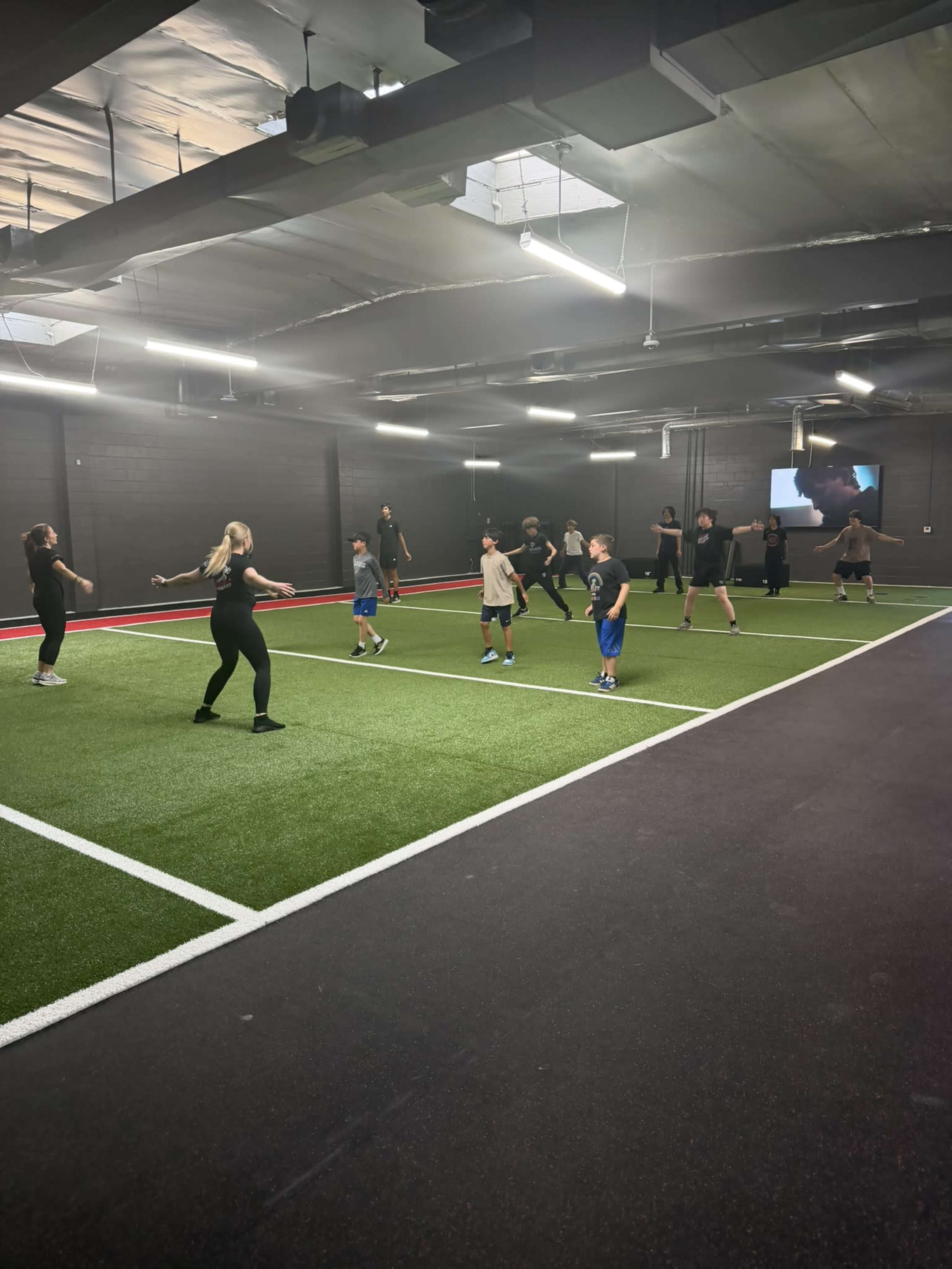A diverse group of people is participating in a fitness class on a synthetic turf surface in a gym.