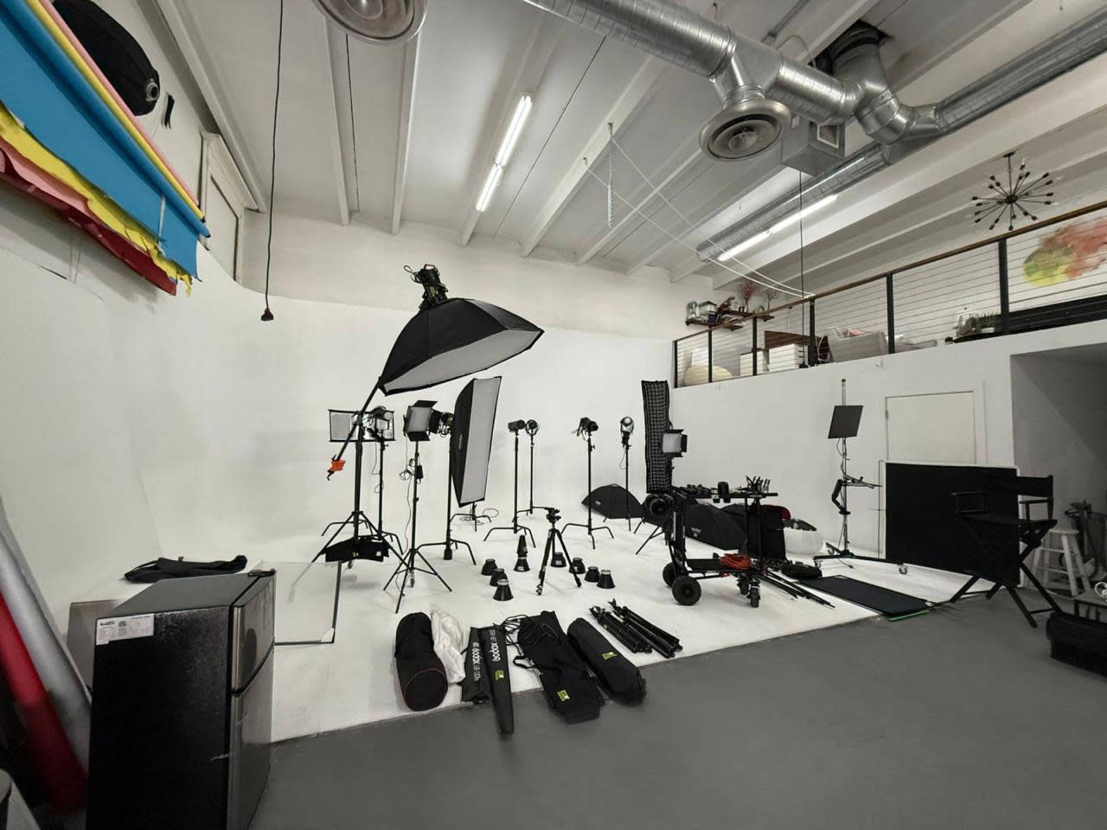 The image shows a photography studio equipped with various lighting setups, stands, and black fabric props arranged on the floor.