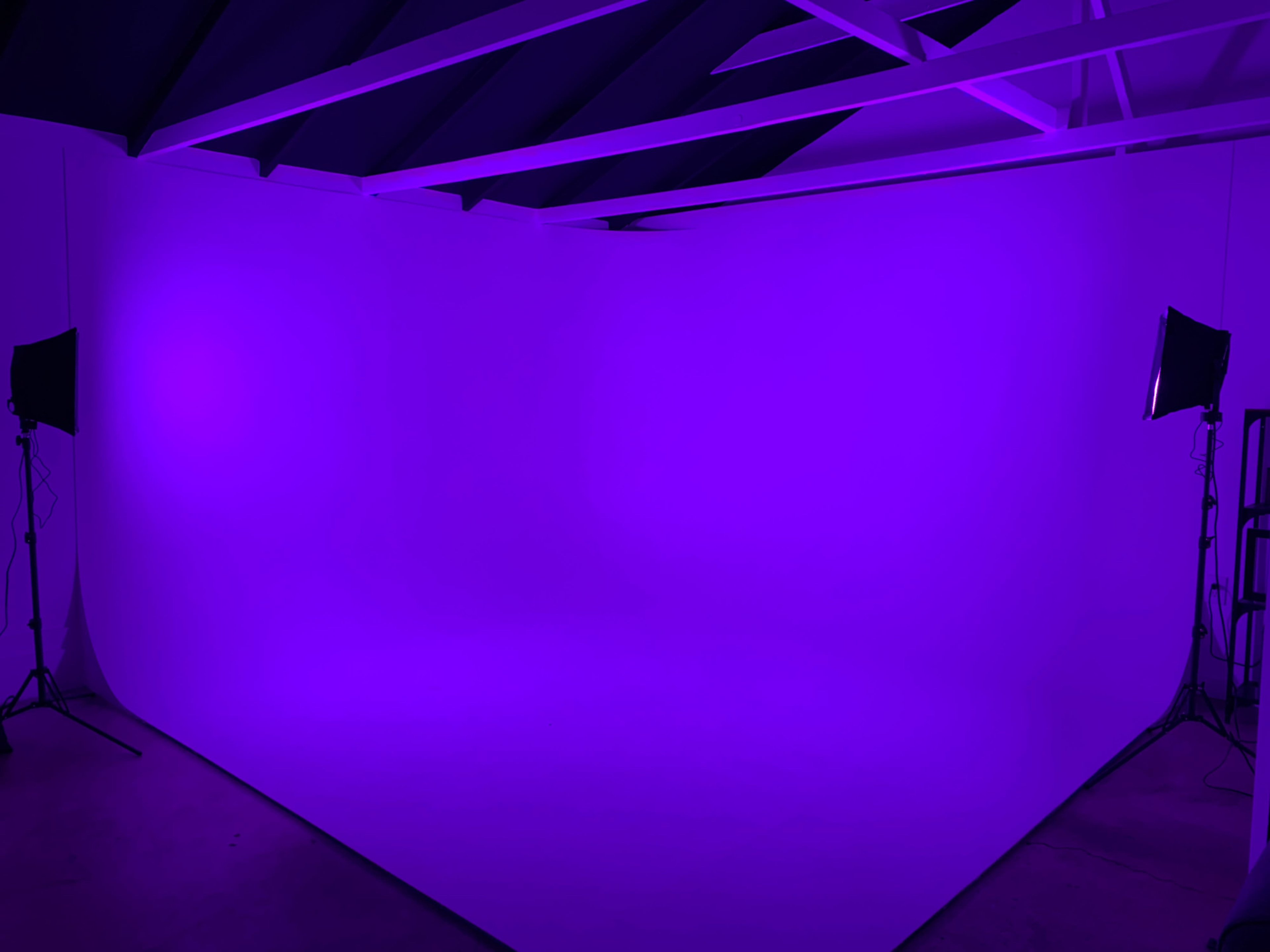 A minimalist studio space with a purple backdrop and lighting, featuring exposed beams on the ceiling.