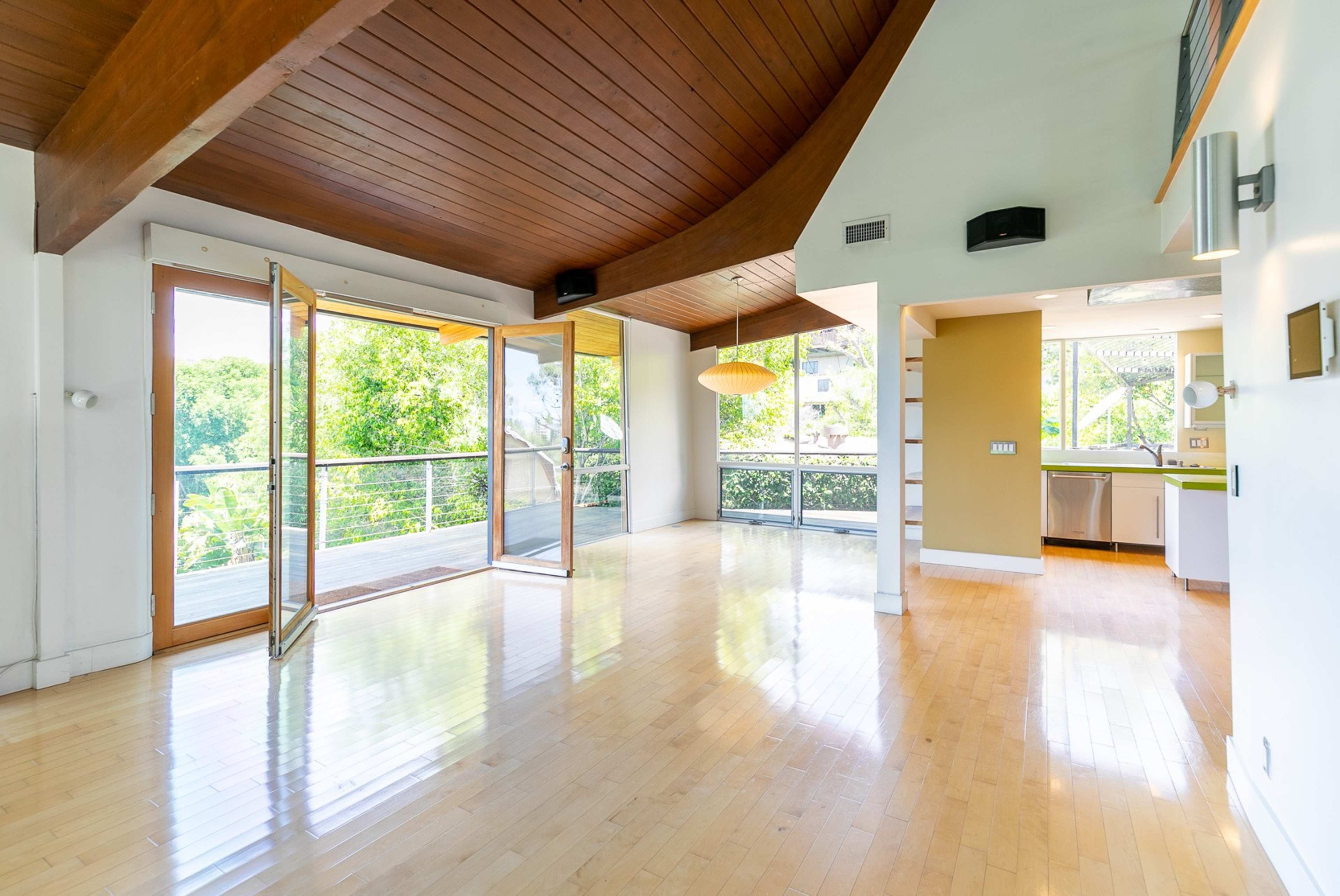 A spacious room features large open doors leading to a balcony and wooden ceilings with a modern light fixture.