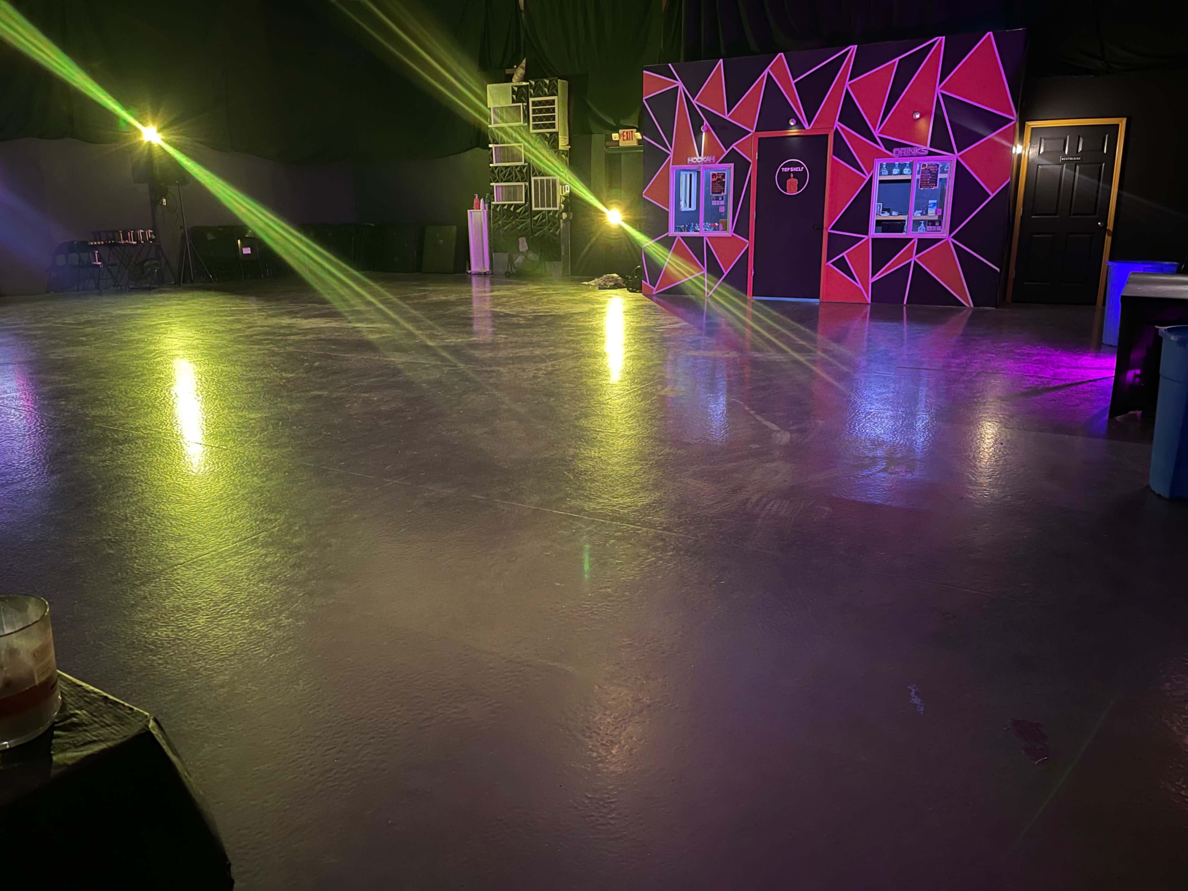 An empty event space with colorful lights illuminating a geometric backdrop and polished concrete flooring.