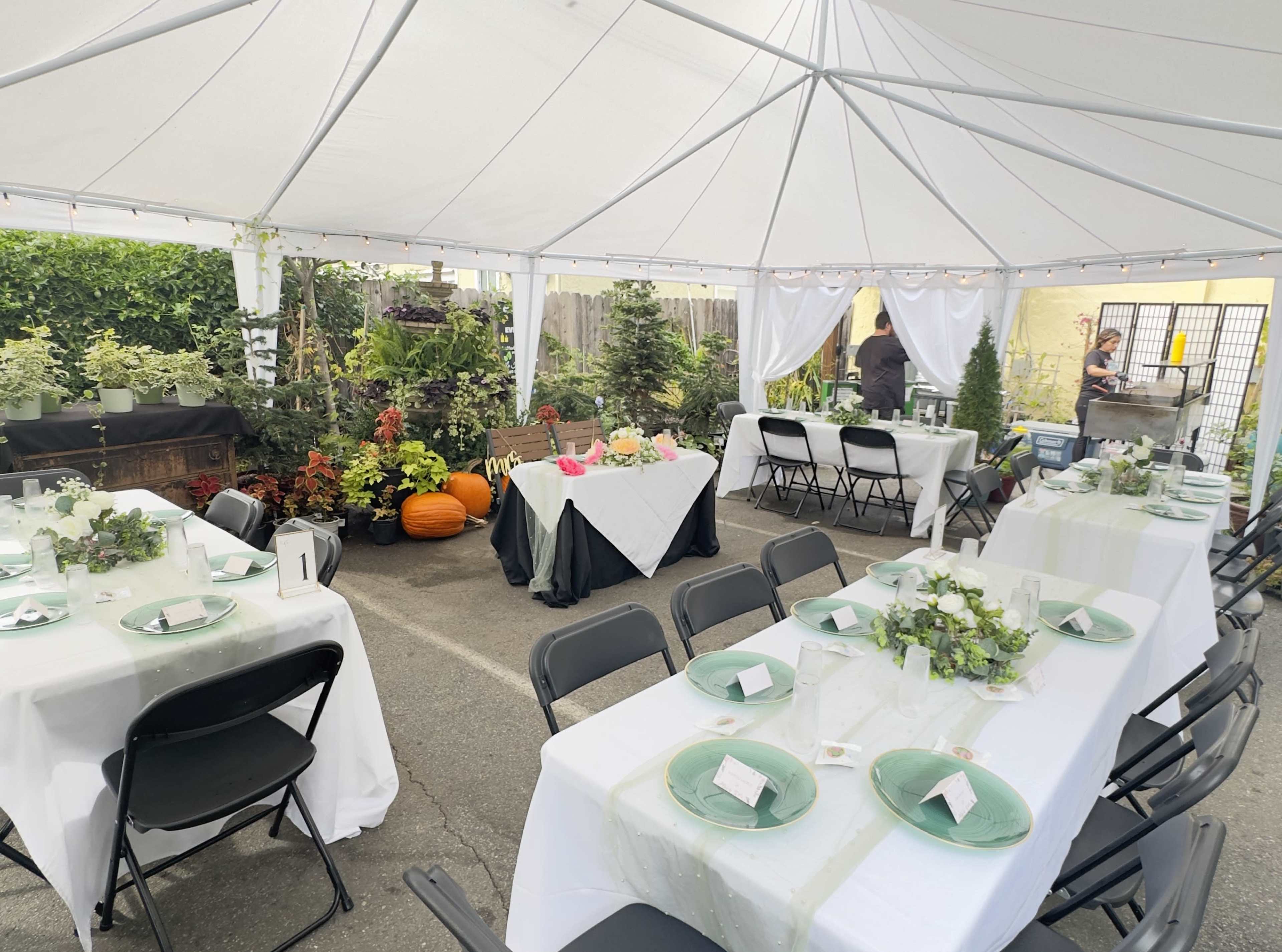A tented outdoor setting features several neatly arranged tables adorned with green plates and centerpieces, alongside a buffet table and decorative pumpkins.