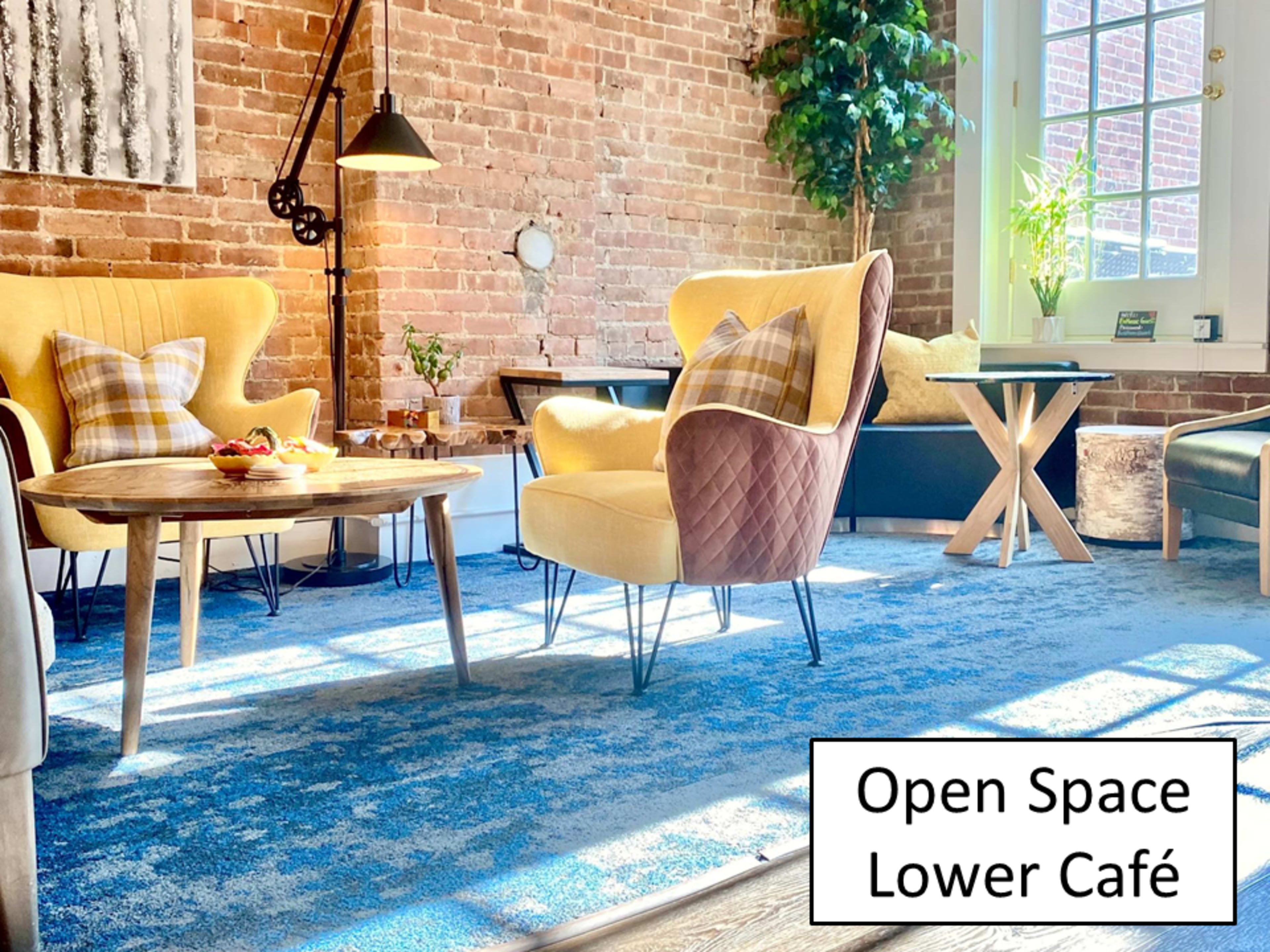 A cozy café with yellow and brown seating, wooden tables, and a patterned blue rug under natural light from large windows.