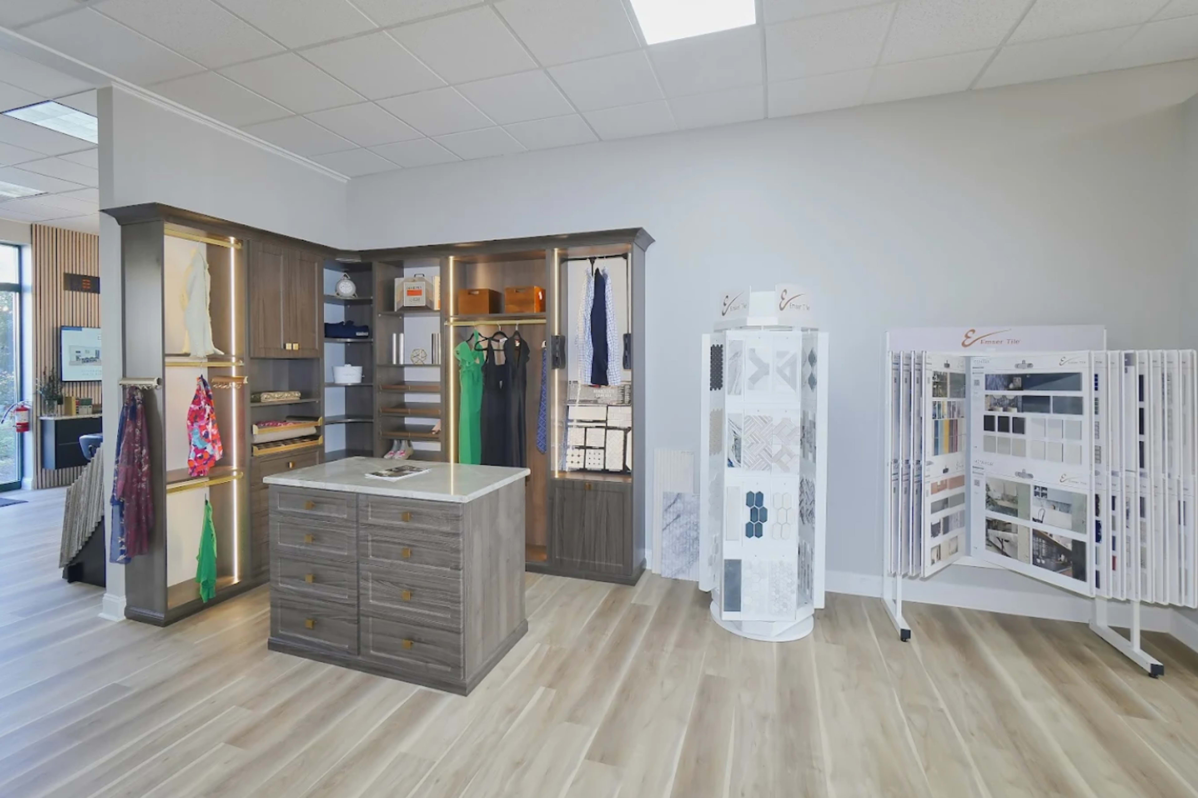 The image shows a modern interior space featuring a display area with clothing racks, storage drawers, and fabric samples arranged on stands.