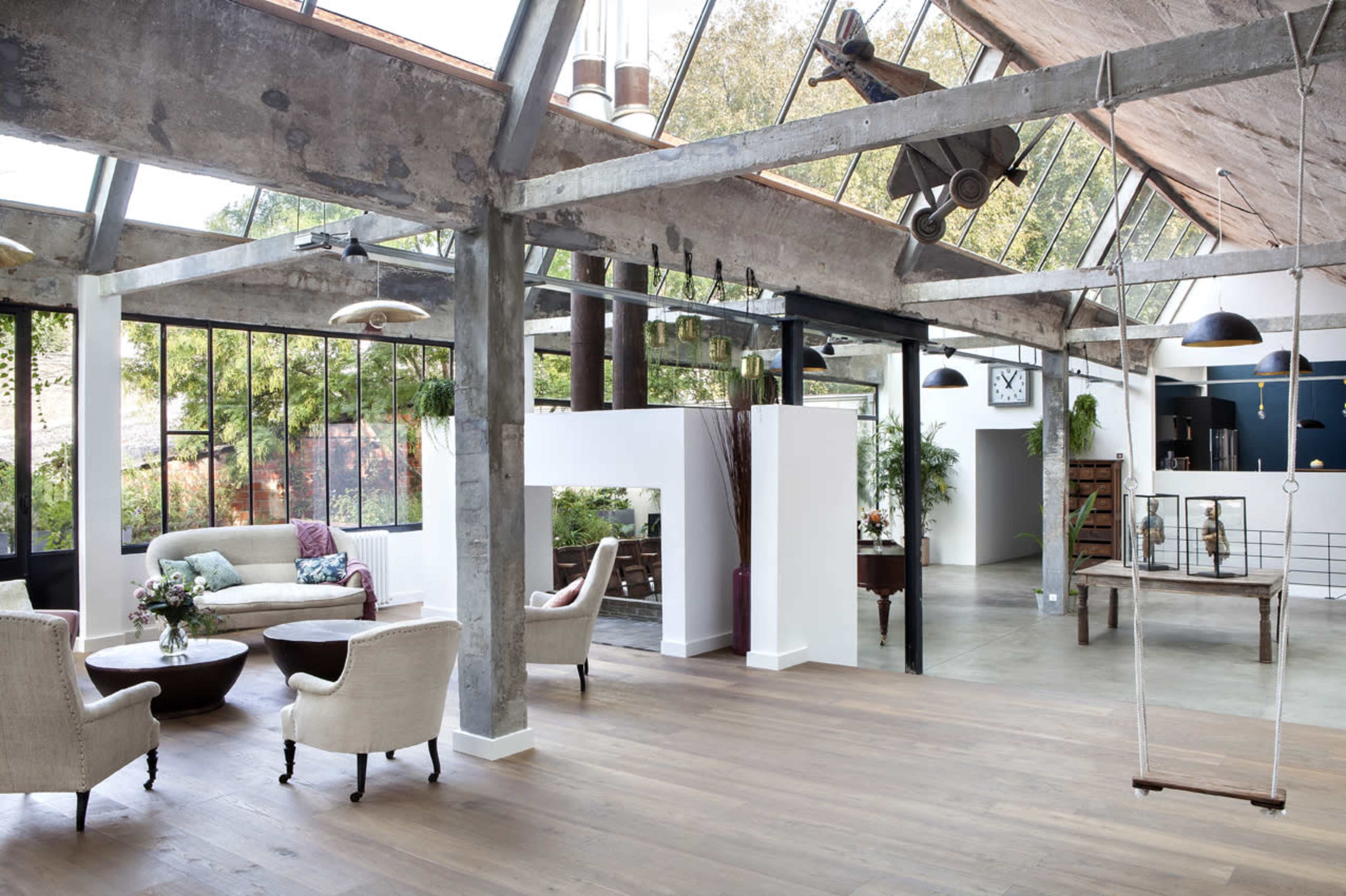 A spacious, open interior with large windows, featuring a seating area with armchairs, a coffee table, and decorative plants.