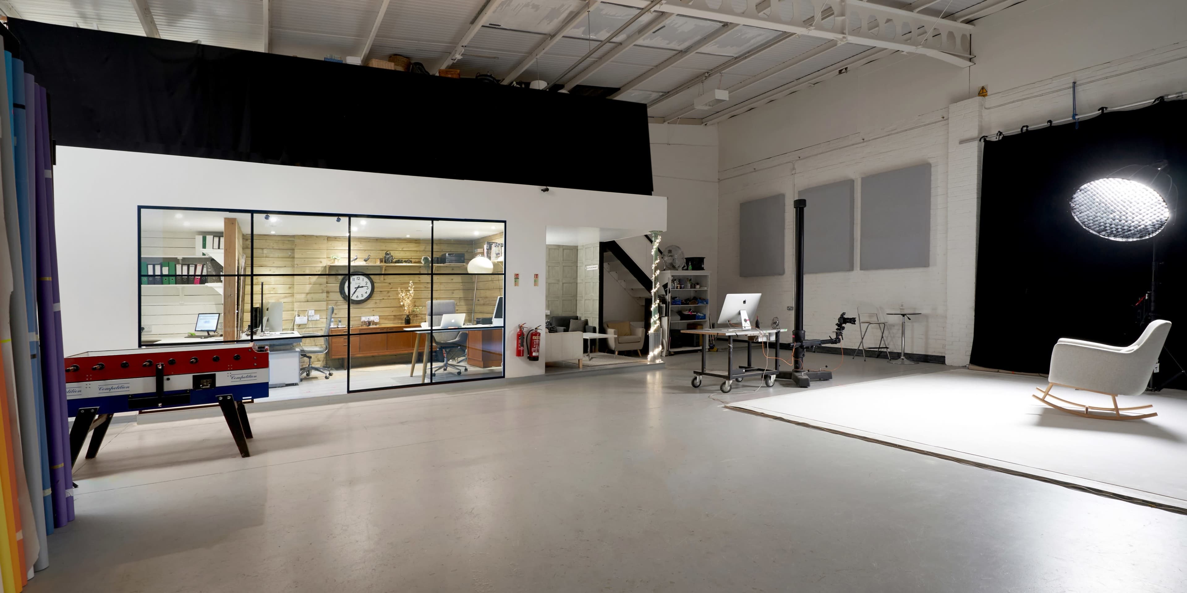 A spacious, modern office area with a glass-walled workspace on one side and an empty photography studio setup on the other.