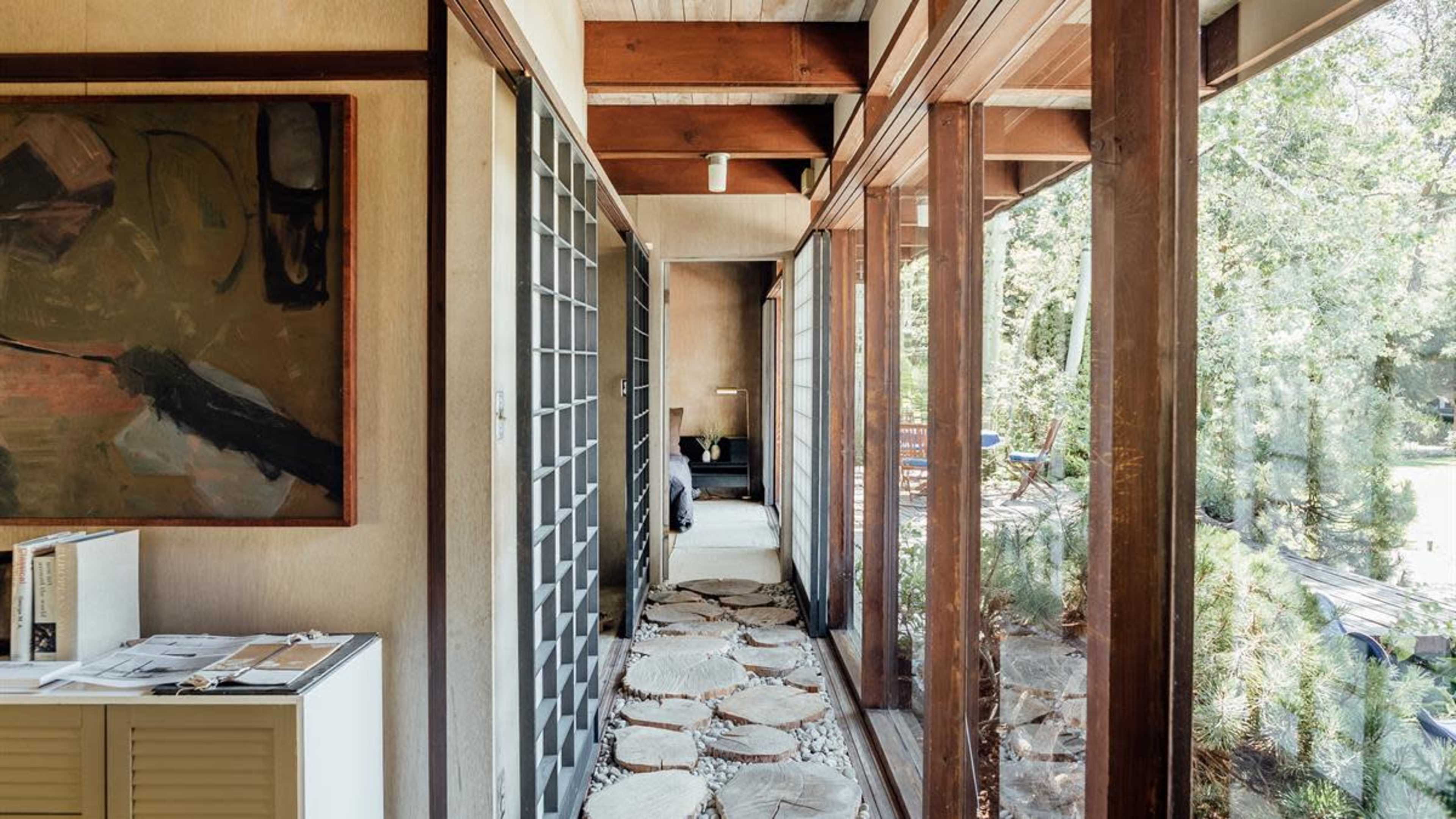 A corridor with large windows framed by wooden beams, featuring a stone path and artwork on the walls.