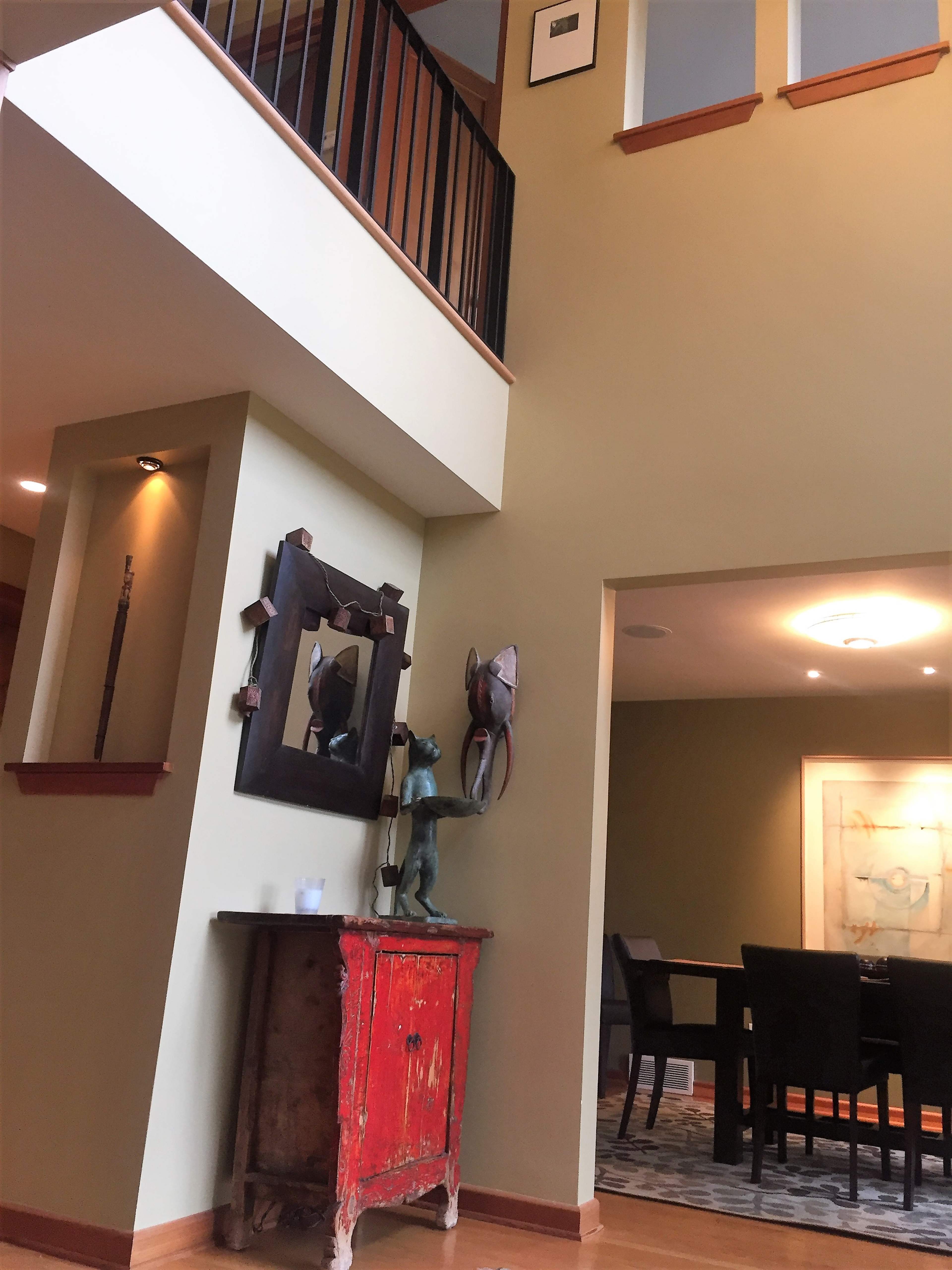 A two-story interior space featuring a red cabinet with a mirror and a decorative figure, leading to a dining area with a black table and chairs.