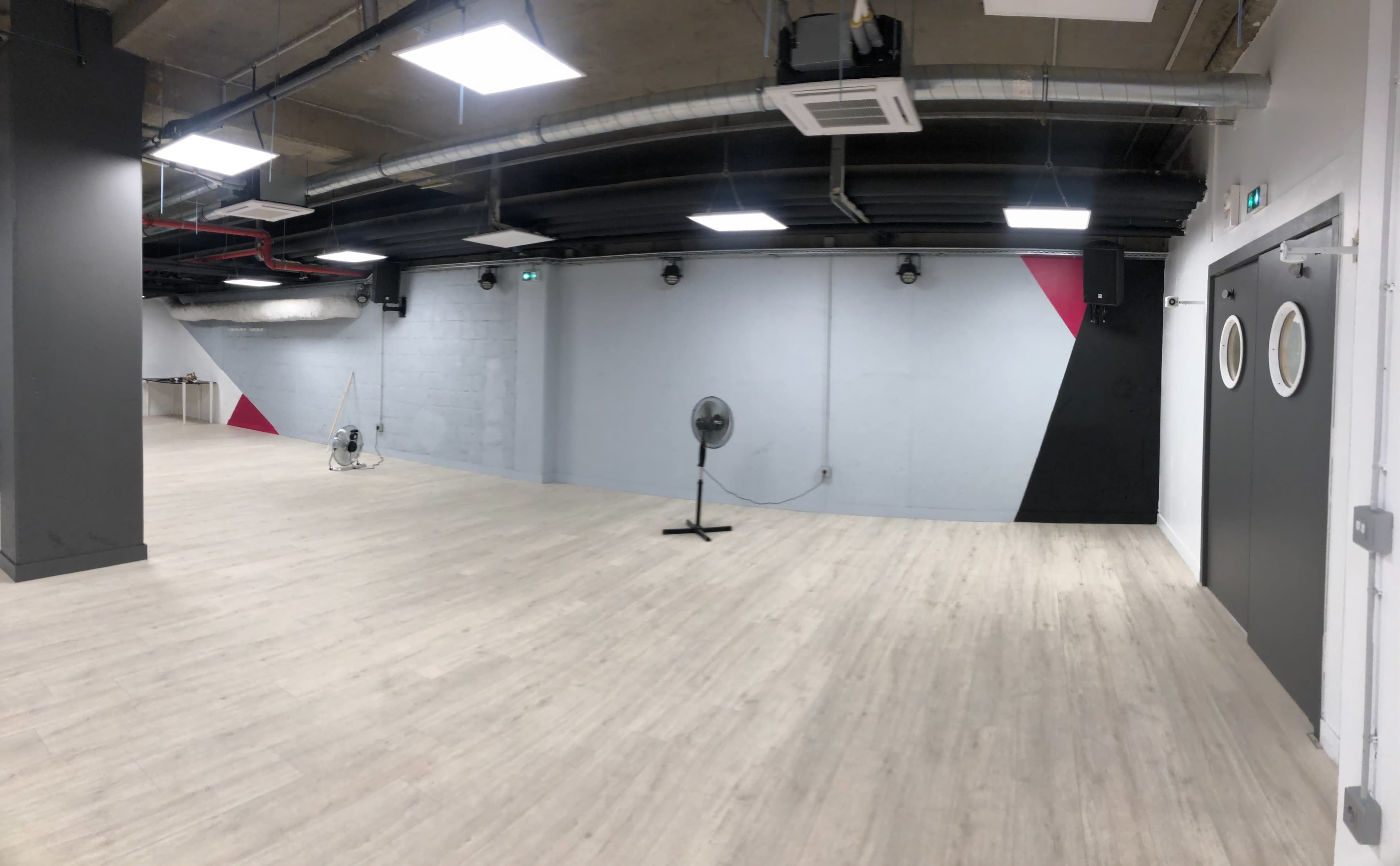 An empty industrial-style room with light wooden flooring and a wall featuring a geometric pattern of black and red sections.